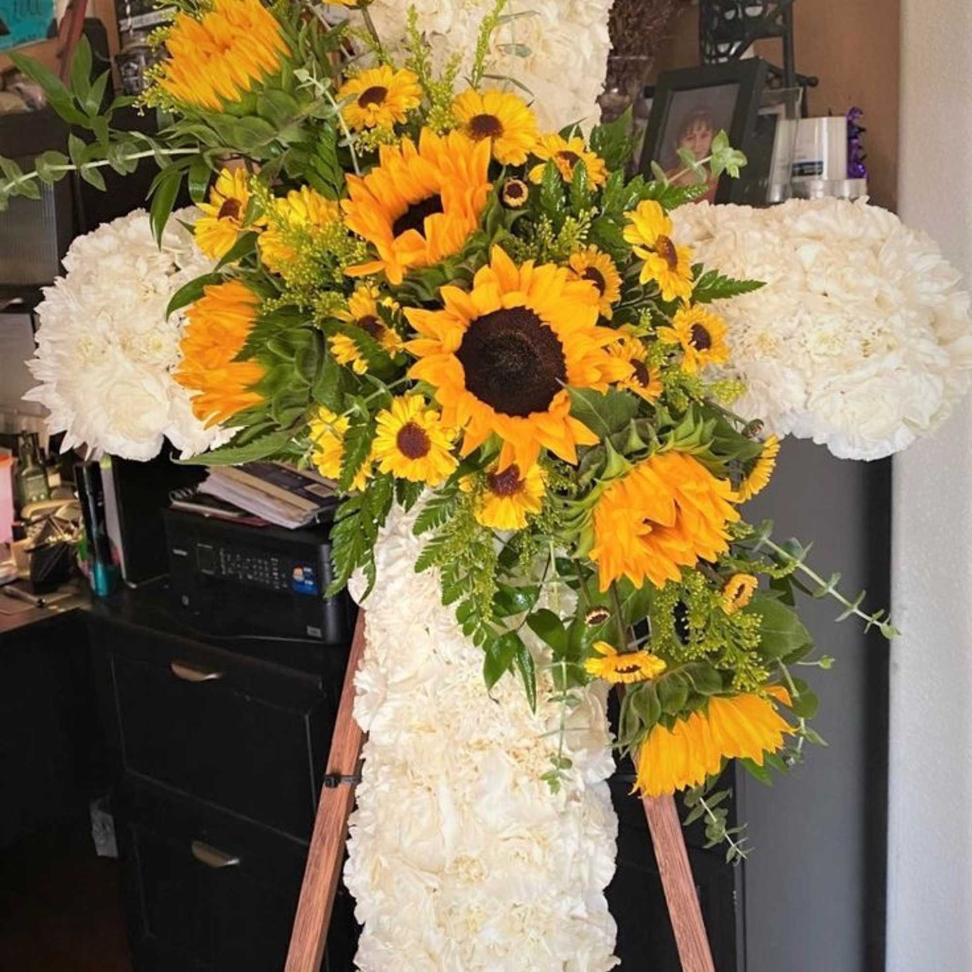 Large floral cross with white flowers and yellow sunflowers on an easel