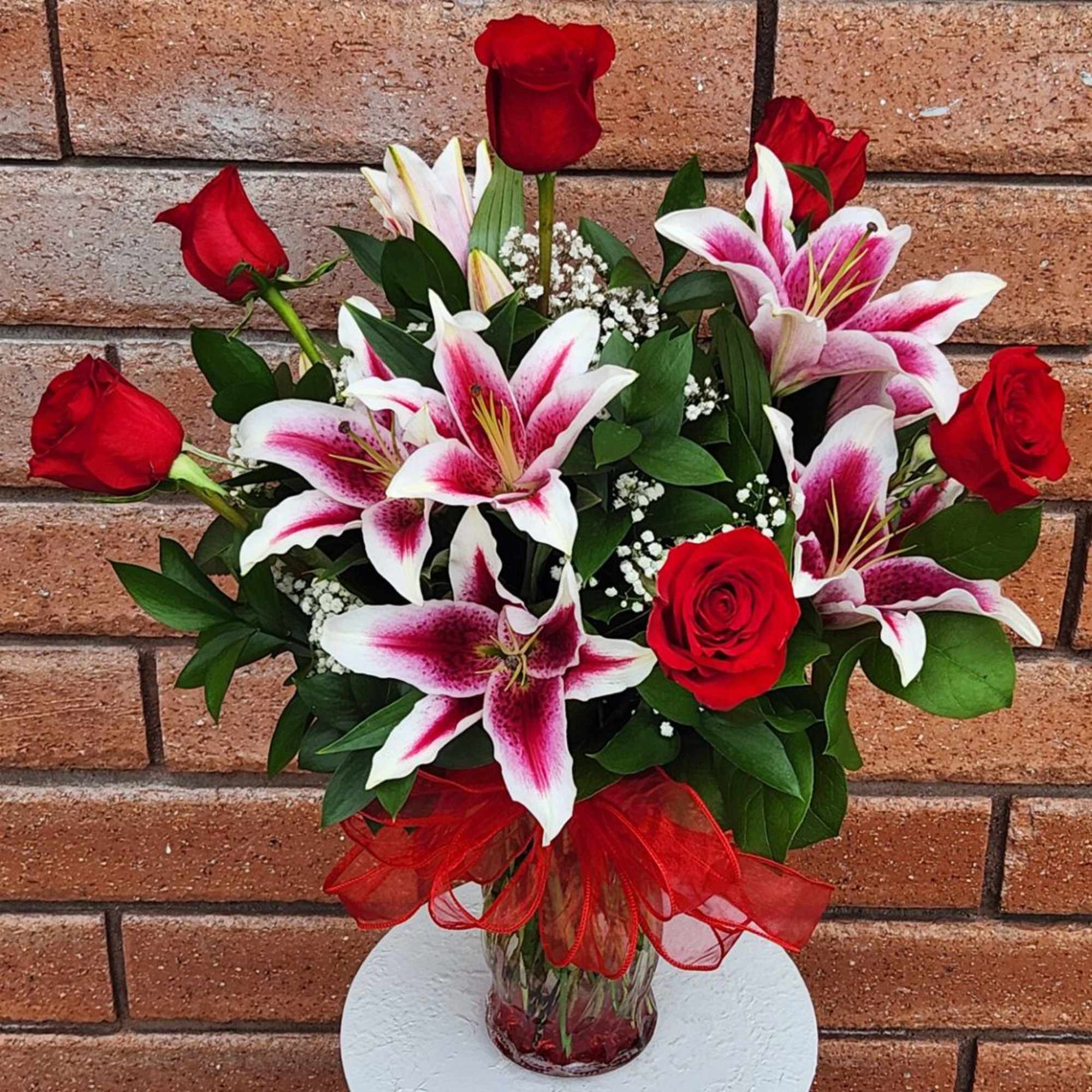 Red roses and pink-white lilies in a glass vase with a red bow
