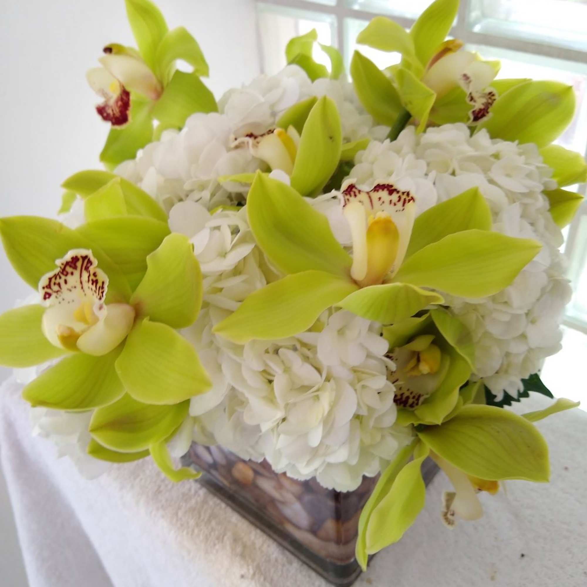 White hydrangeas with lime green orchids in a square glass vase