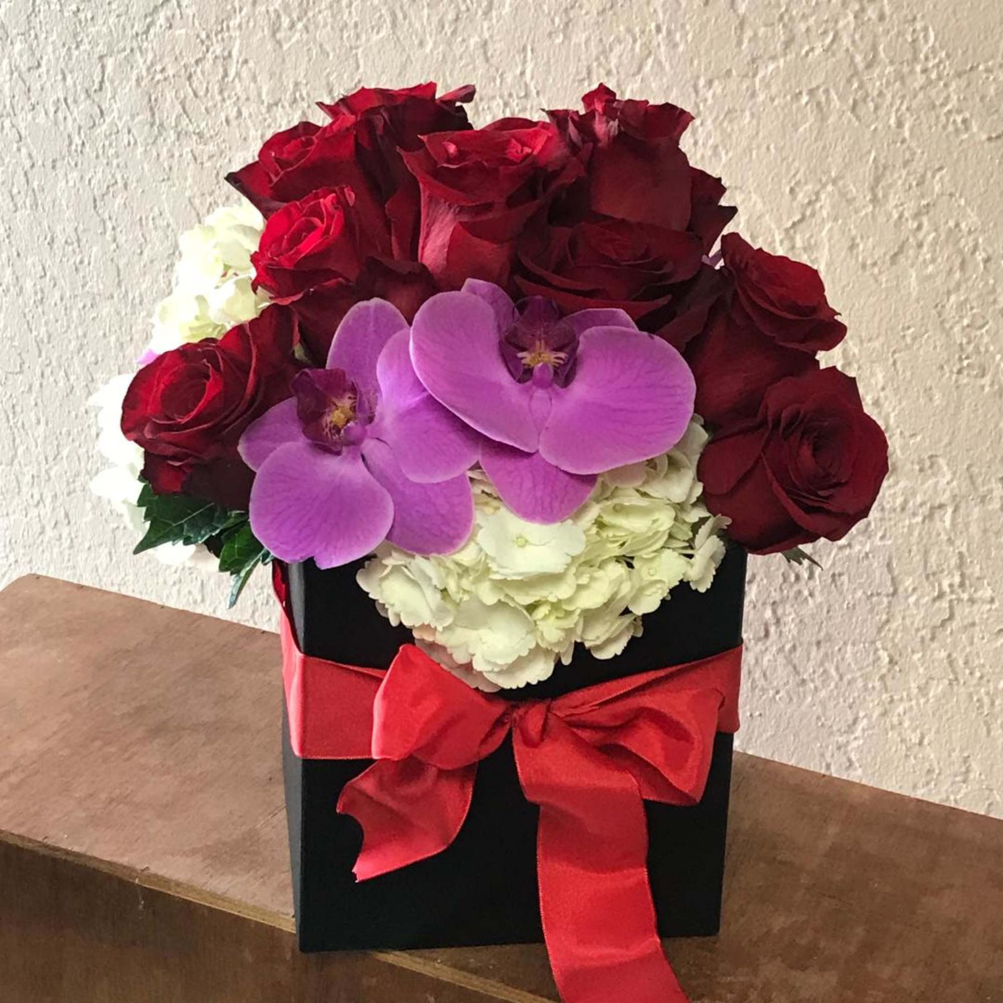 Red roses and purple orchids arranged in a black box with a red ribbon