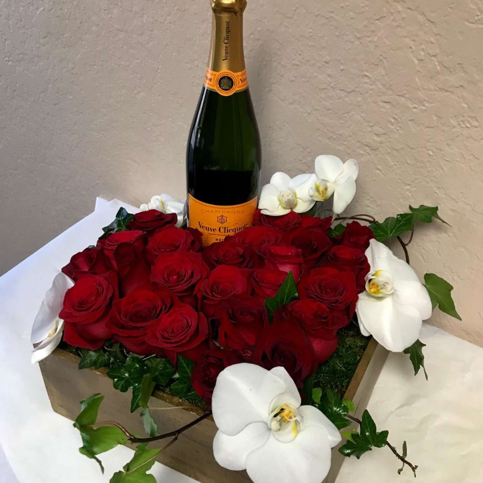 Red roses and white orchids arranged around a champagne bottle in a box