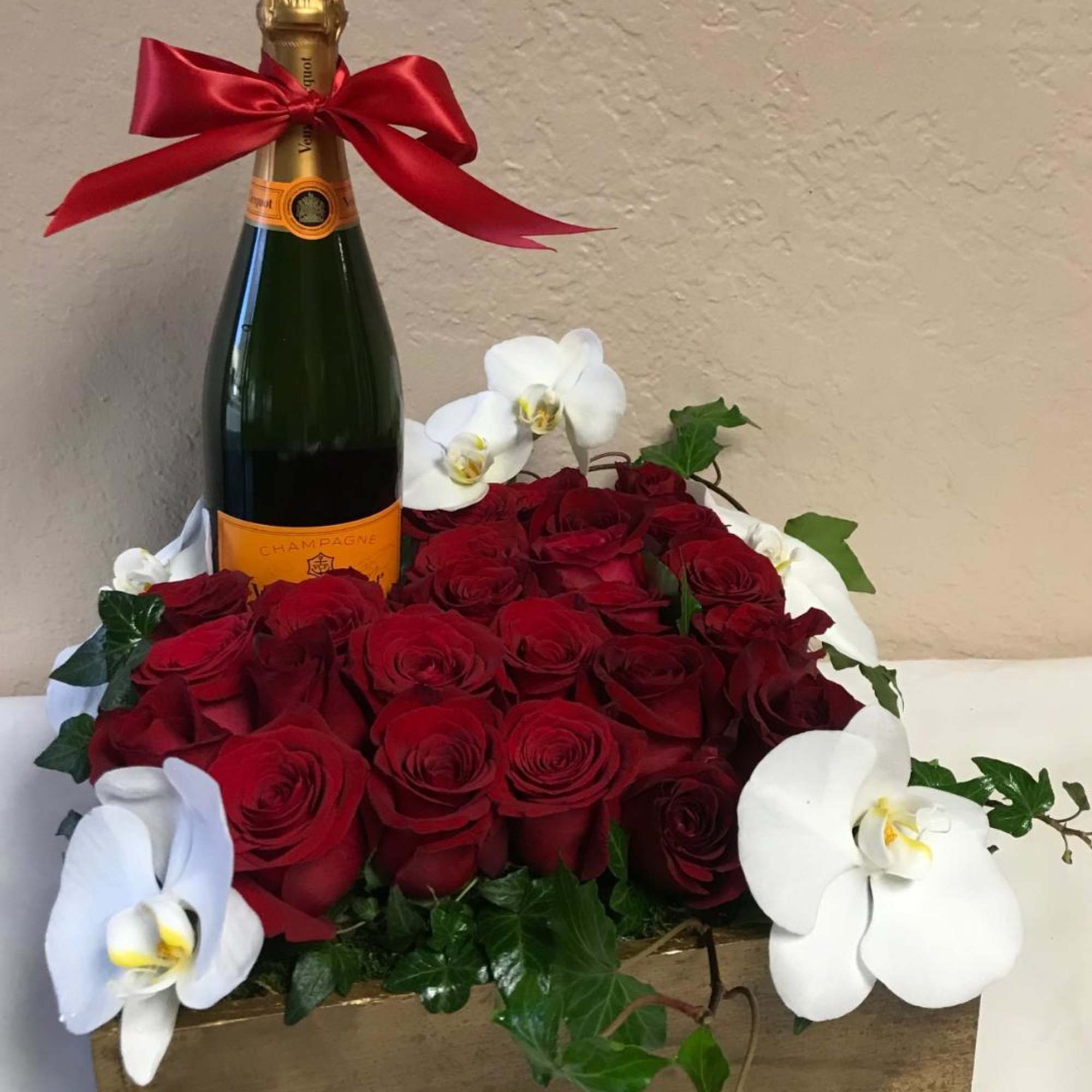 Red roses arranged around a champagne bottle with white orchids
