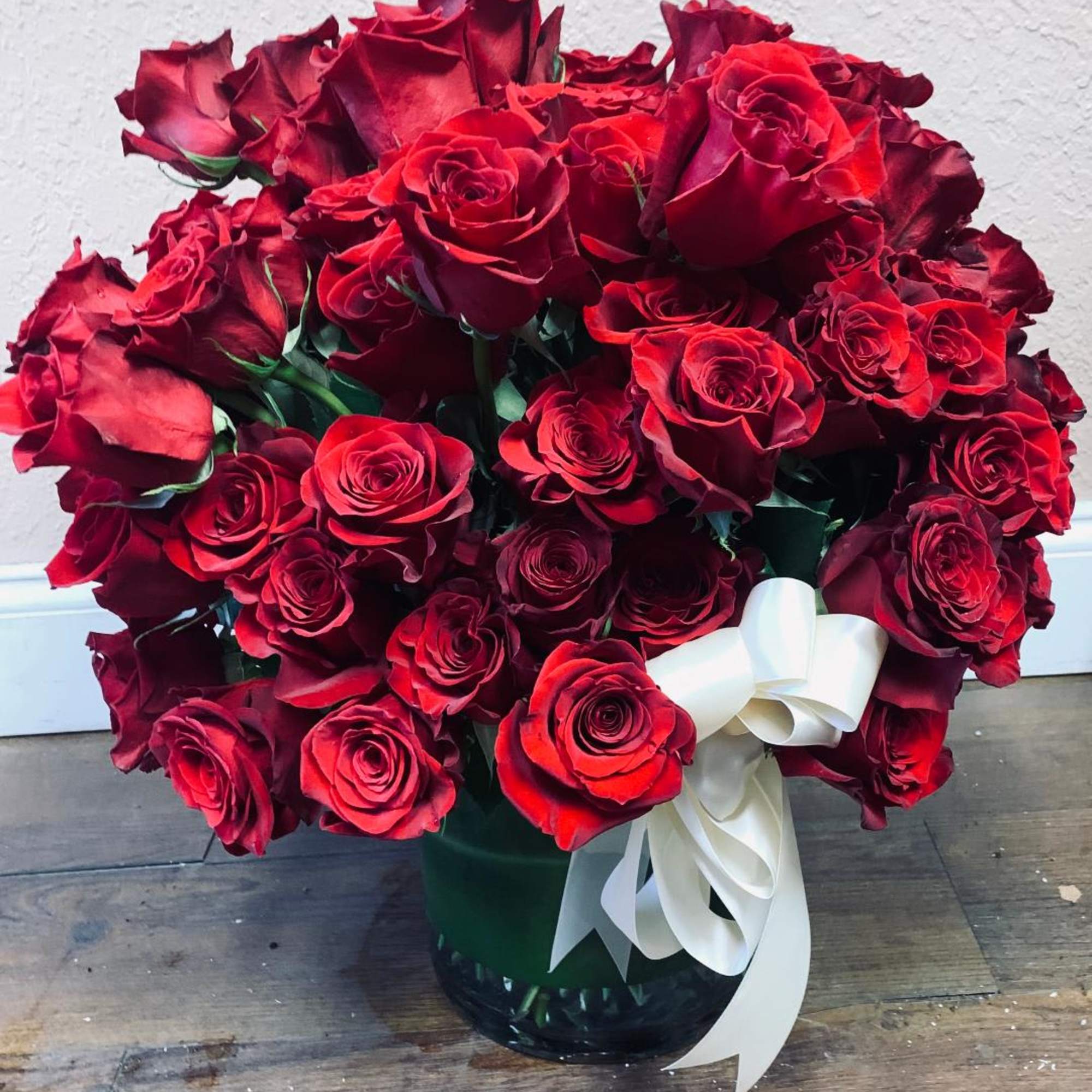 A large bouquet of red roses in a glass vase with a white ribbon