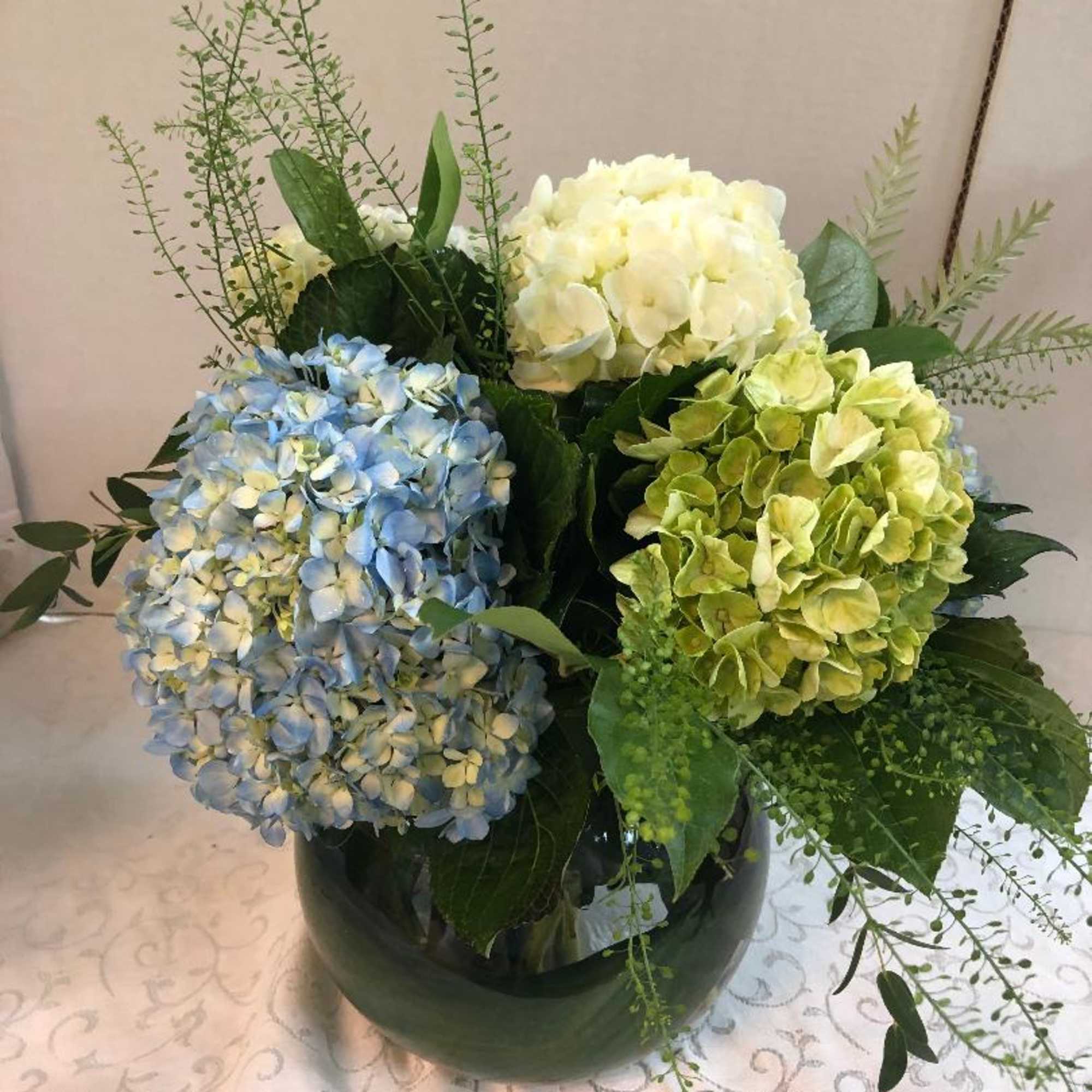 Hydrangea arrangement in a dark vase with blue, white, and green blooms