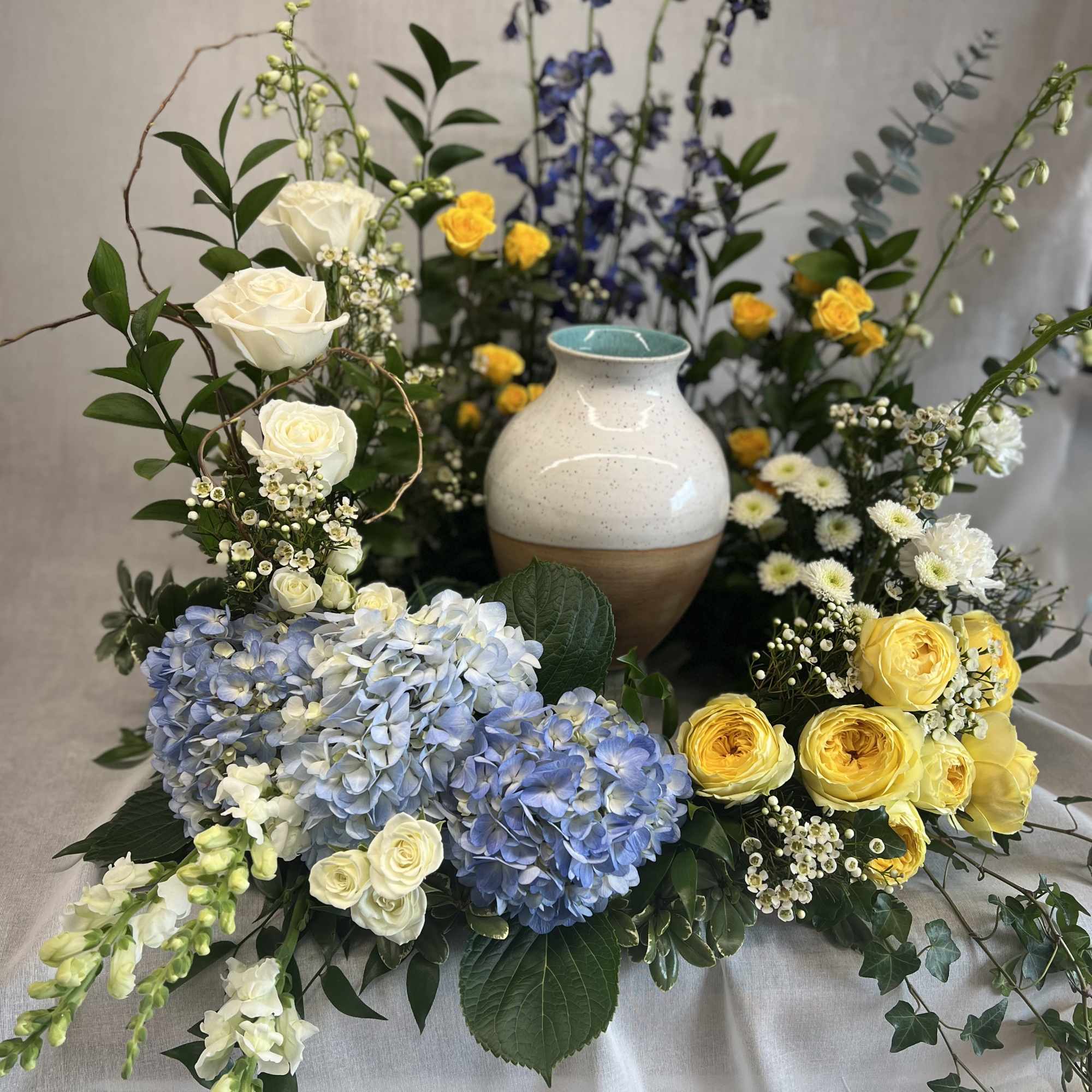 Floral arrangement with blue hydrangeas, yellow roses, and white roses around a ceramic vase