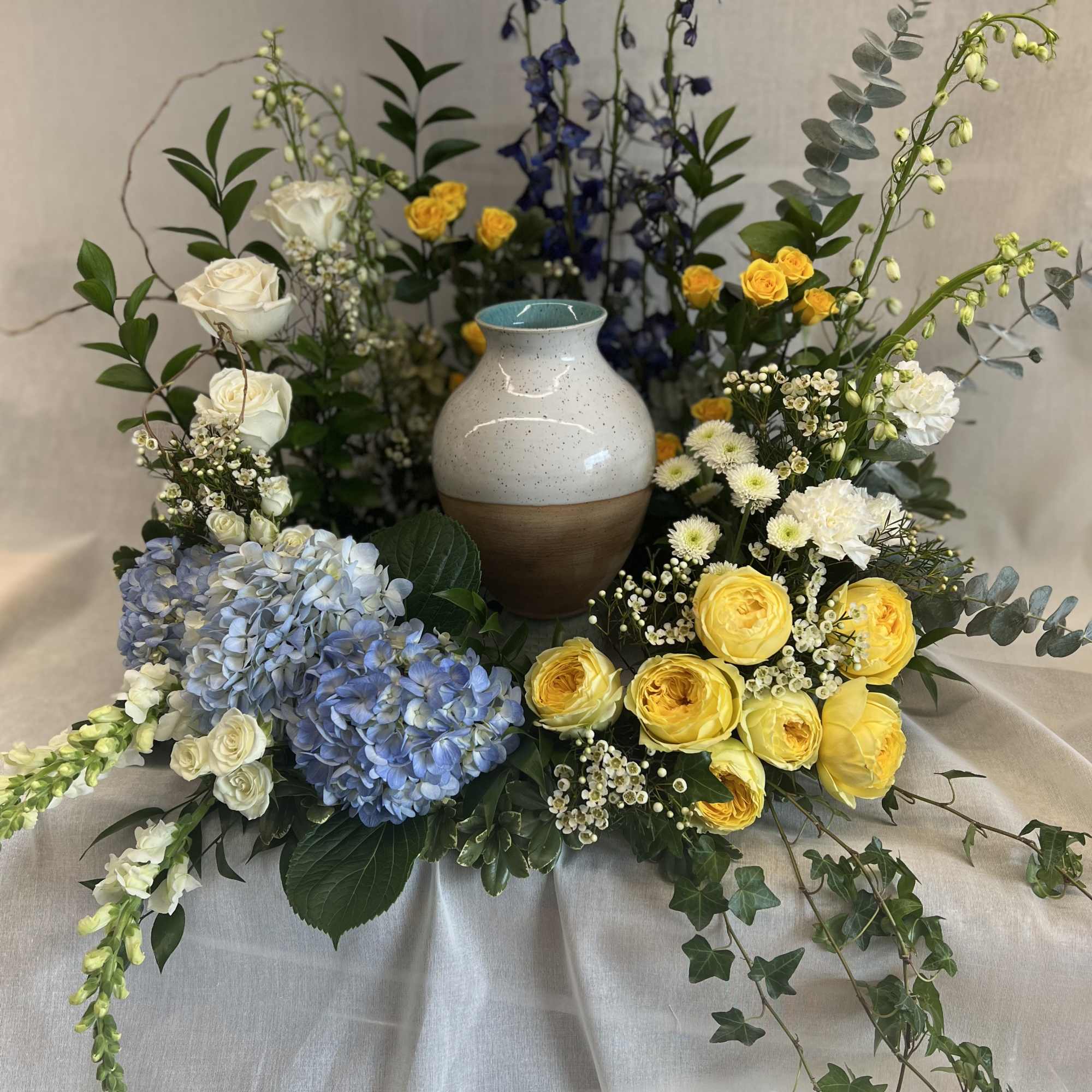 Floral arrangement with yellow and white roses, blue hydrangeas, and a ceramic vase
