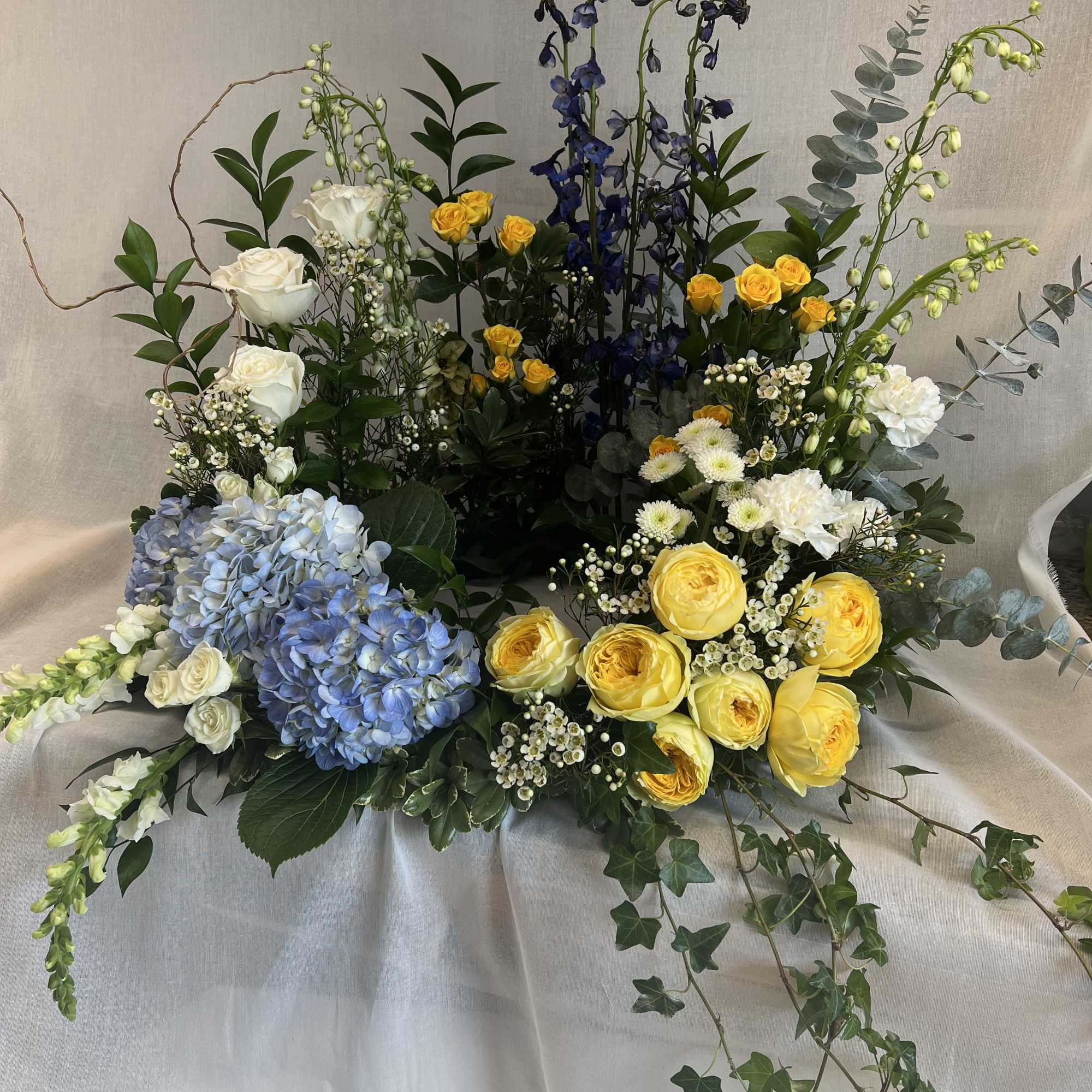 Large floral arrangement with yellow and white roses, blue hydrangeas, and tall blue blooms
