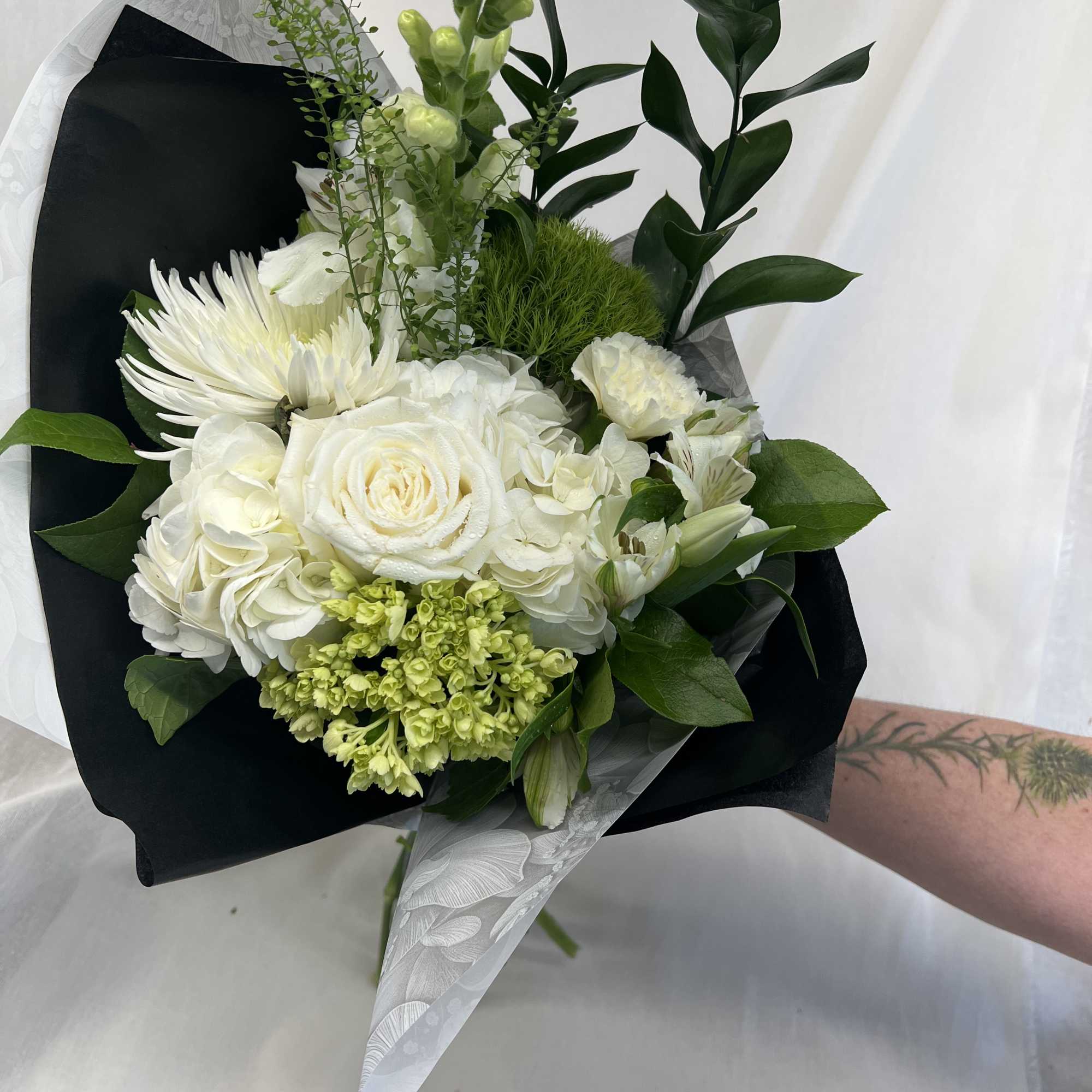 White bouquet with roses, hydrangeas, and chrysanthemums wrapped in black paper