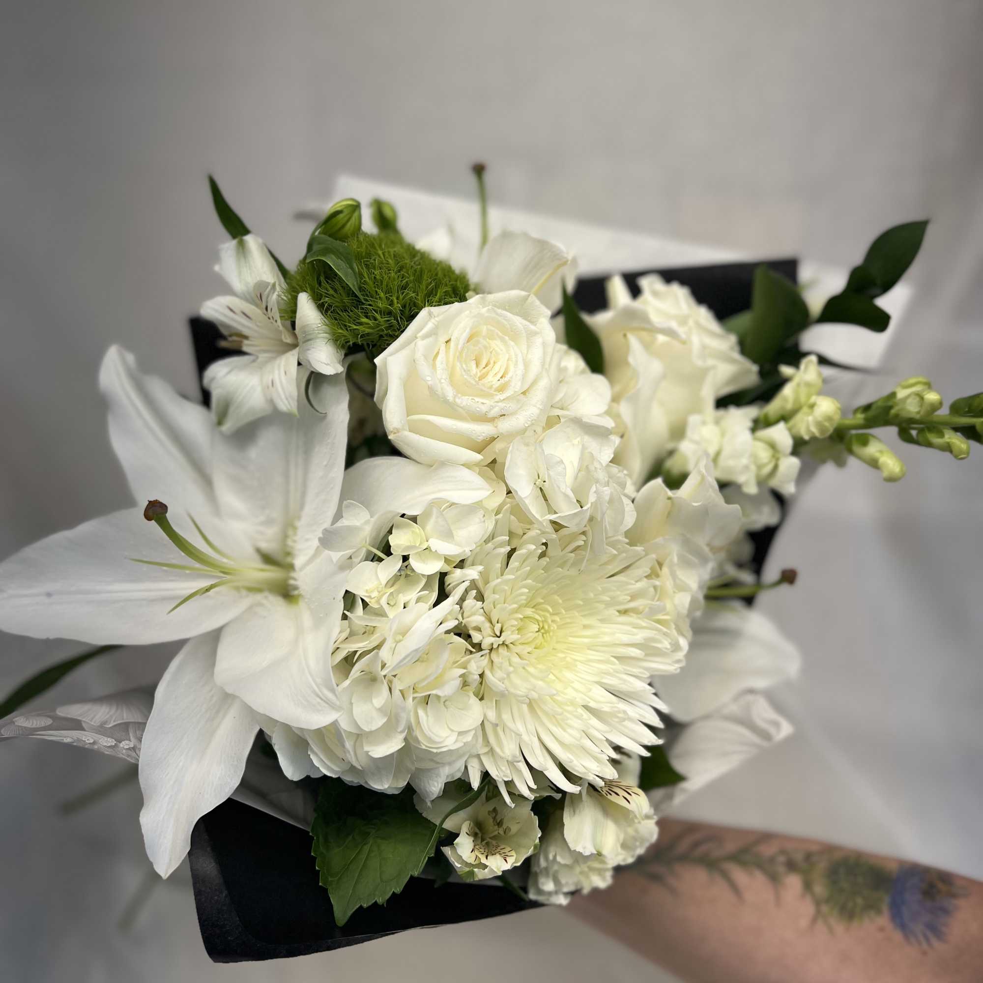 White bouquet with lilies, roses, and chrysanthemums wrapped in black paper