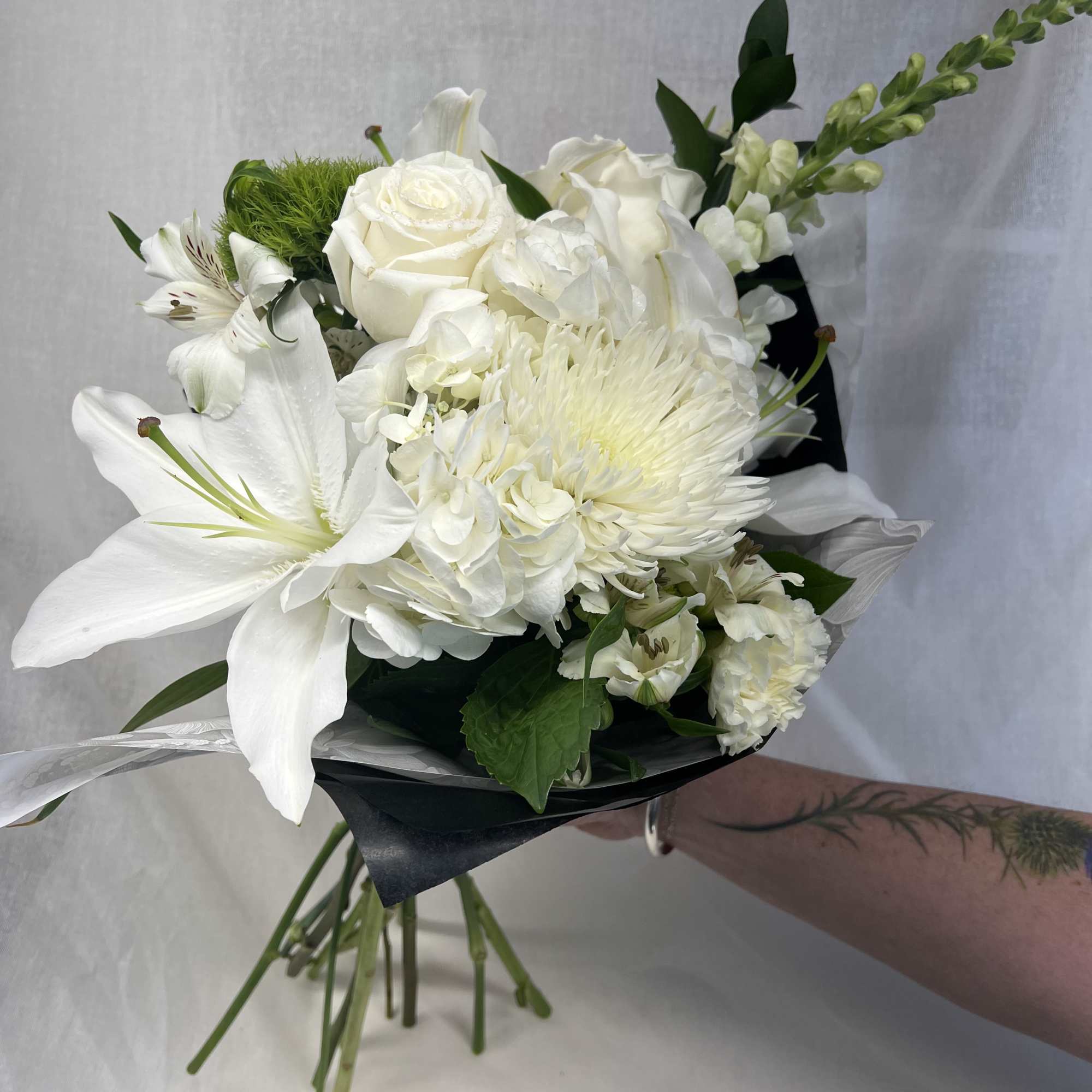 White bouquet with lilies, roses, and chrysanthemums wrapped in dark paper