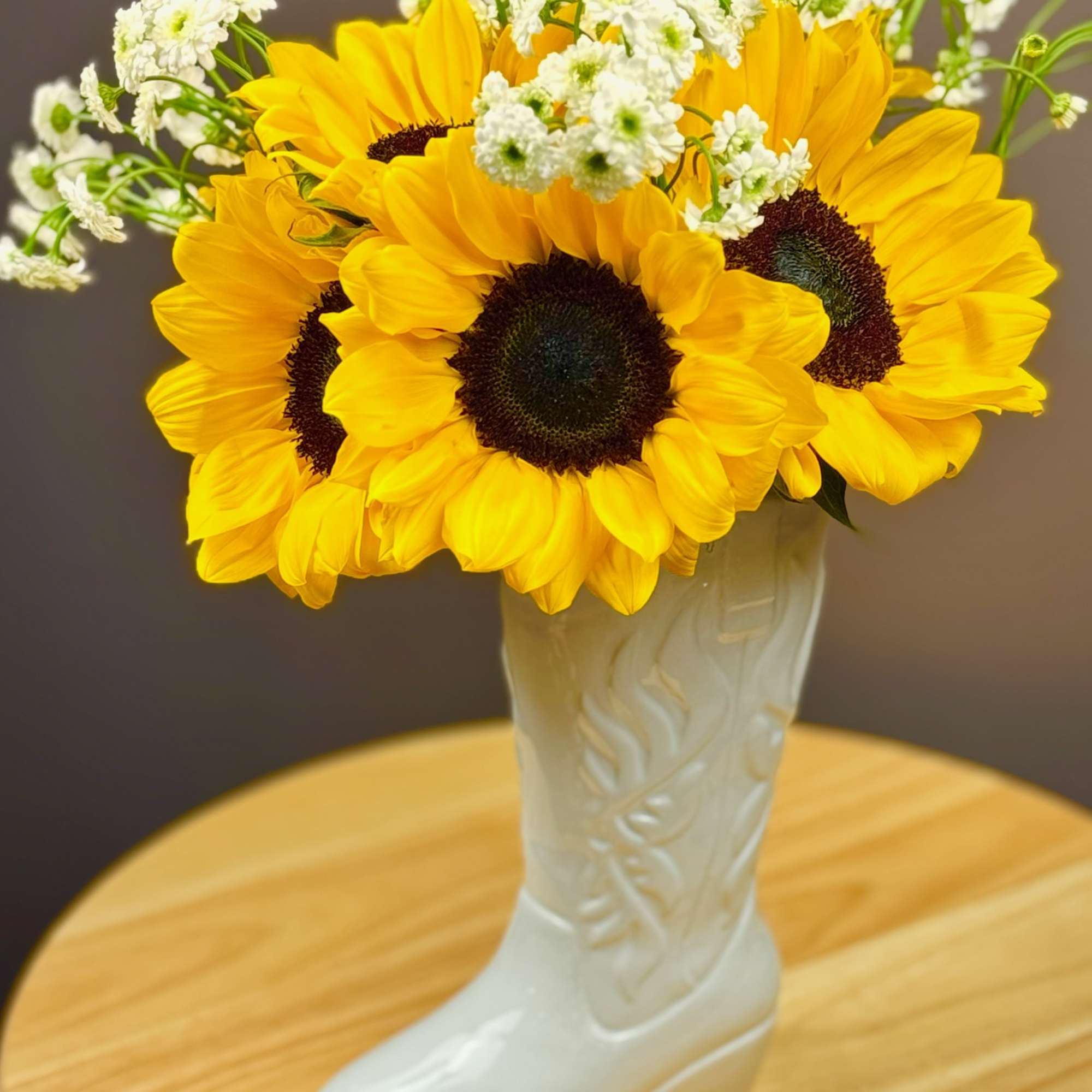 Sunflowers and white filler flowers arranged in a white boot vase