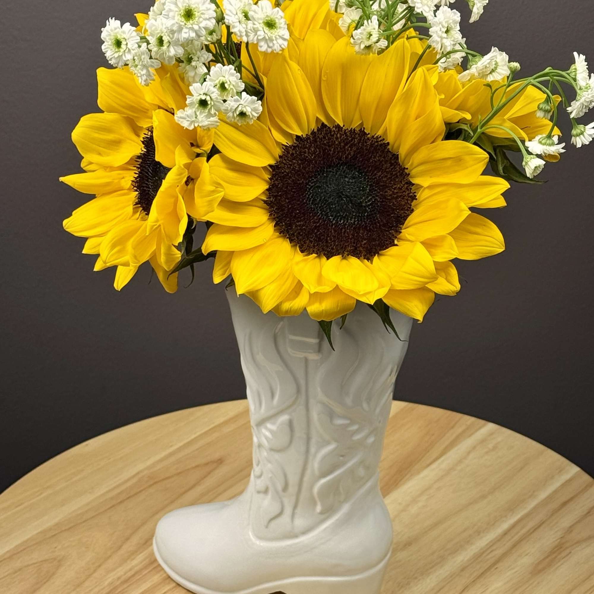 Sunflowers and small white daisies in a white boot-shaped vase