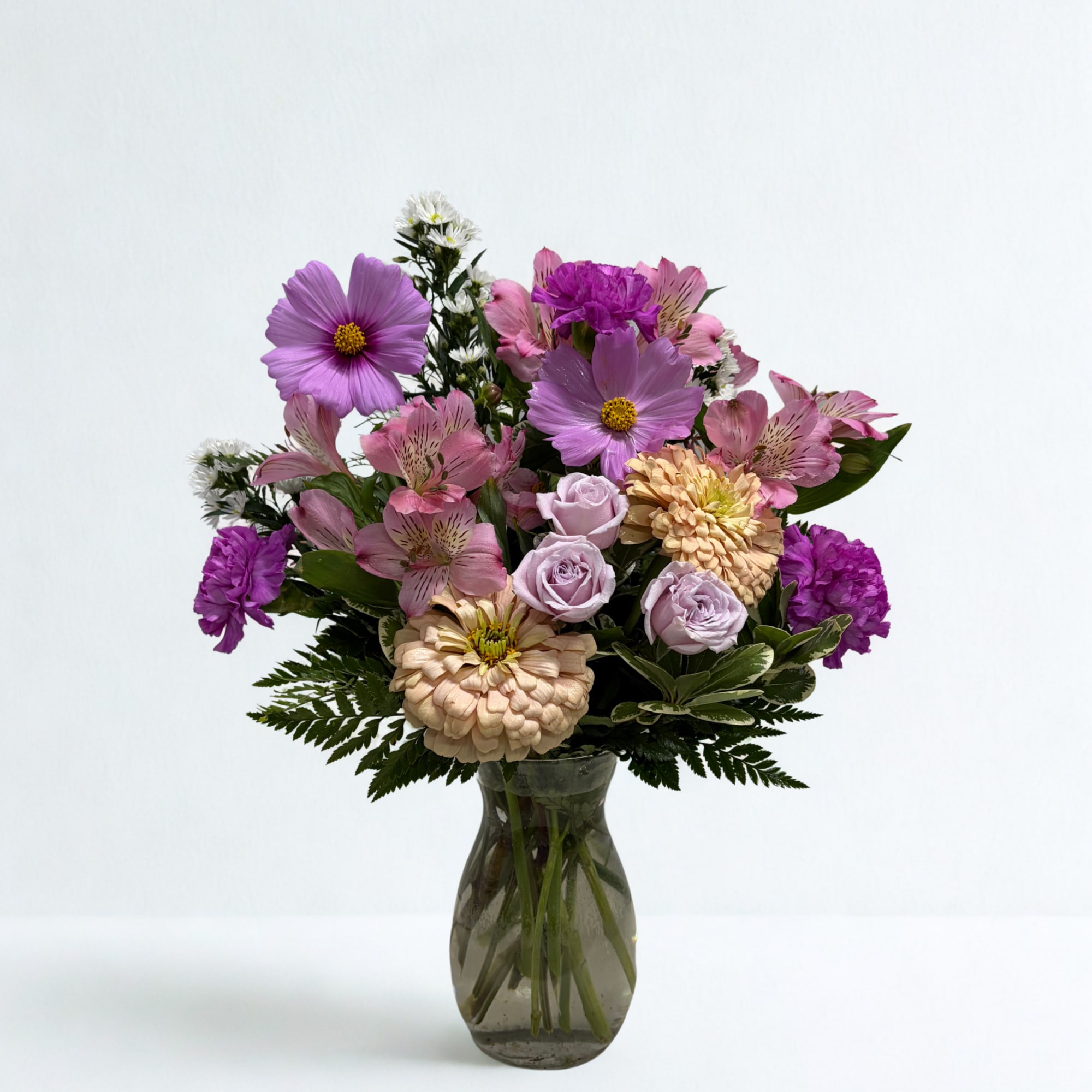 Mixed pink and purple flowers arranged in a glass vase