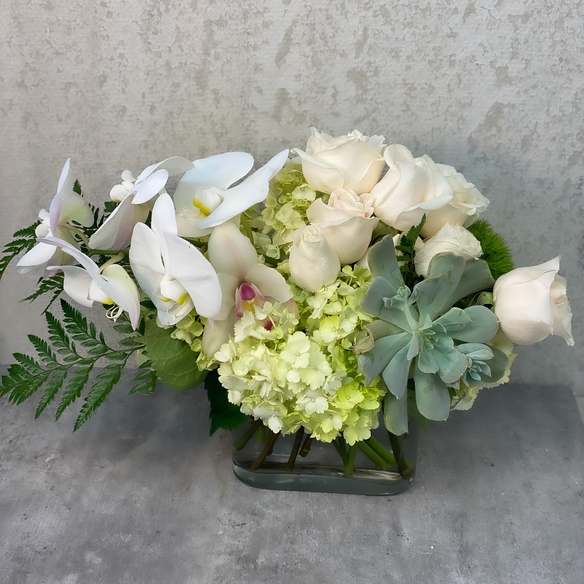 White orchids and roses arranged in a glass vase with pale green hydrangea