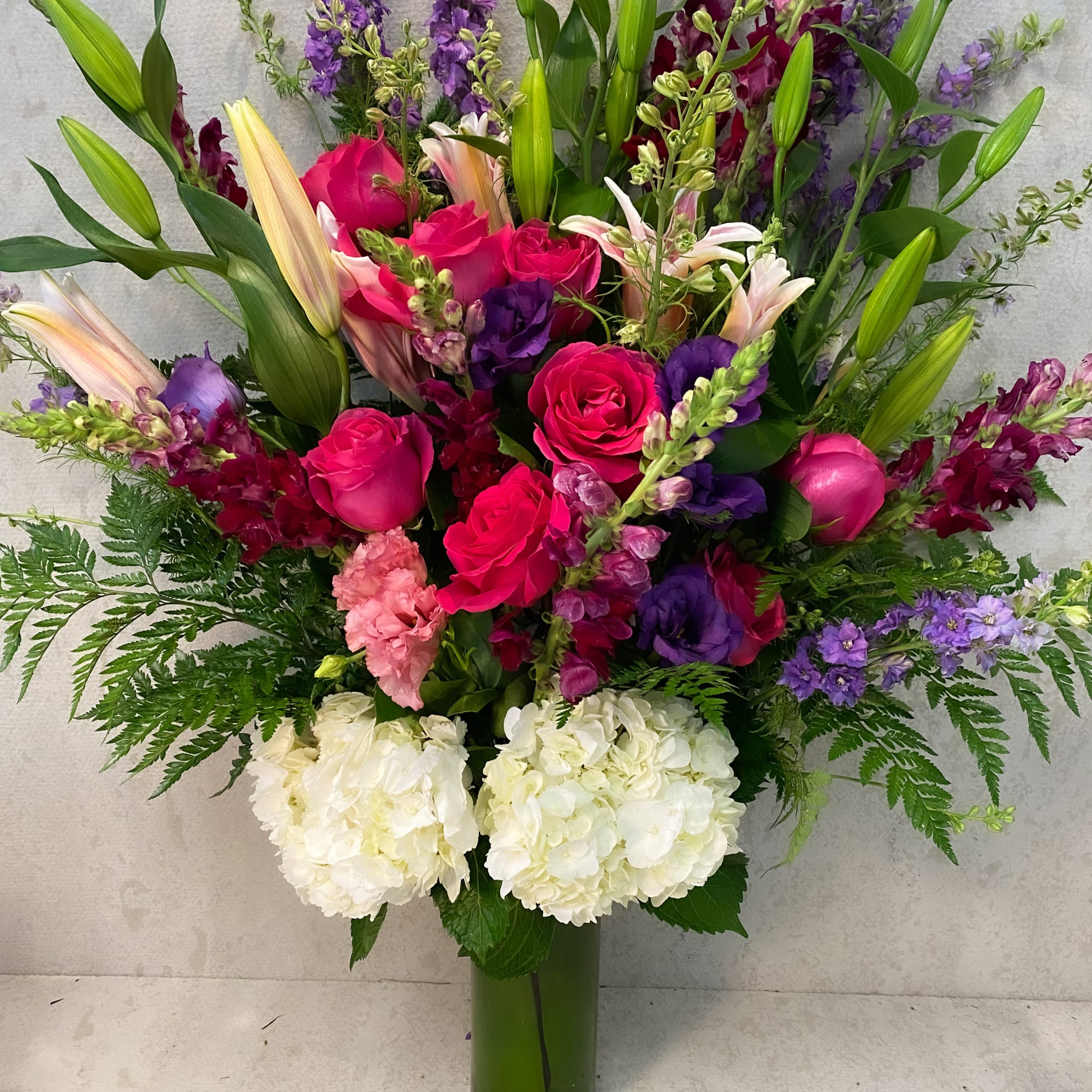 Tall bouquet of pink roses, lilies, and purple flowers in a glass vase