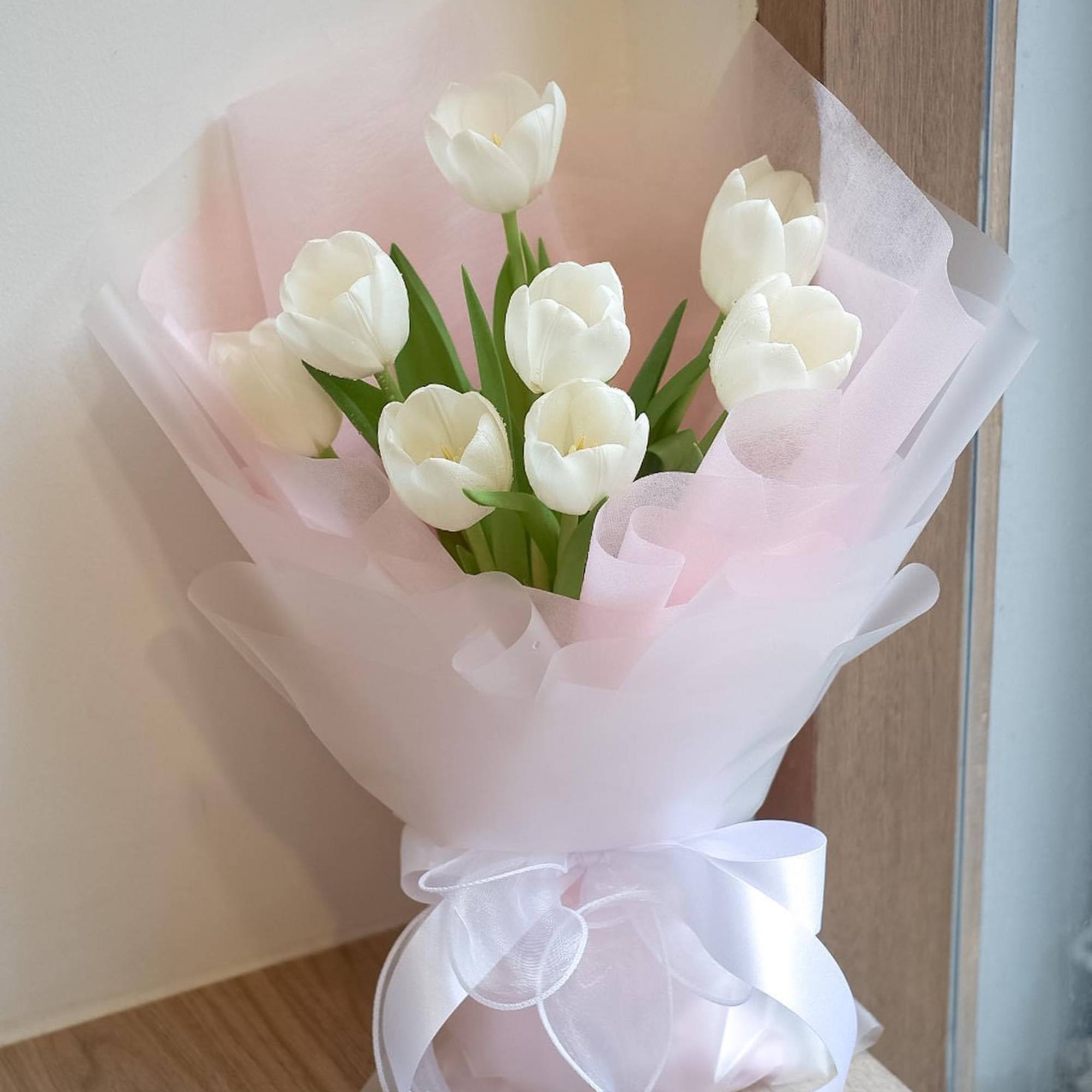 White tulip bouquet wrapped in pale pink paper with a white ribbon