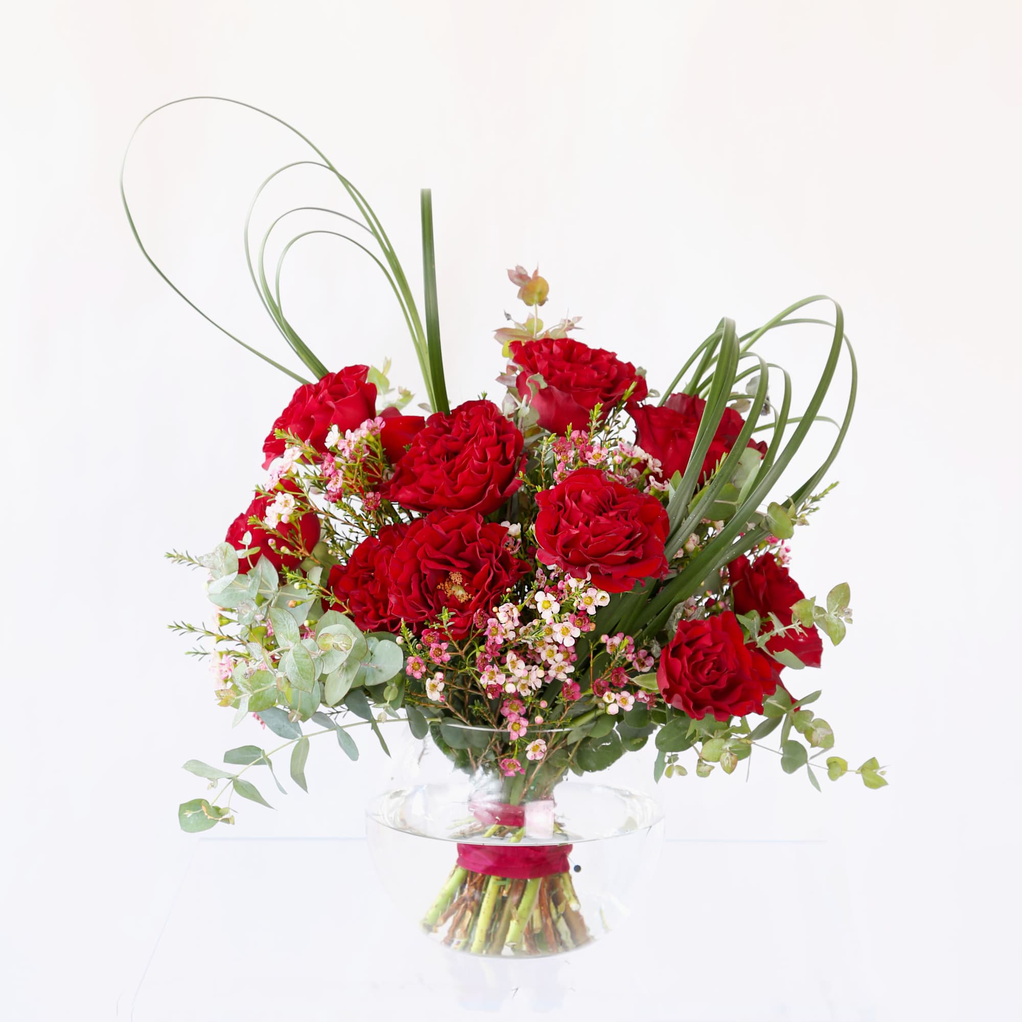 Round arrangement of red roses with pink filler flowers in a clear glass bowl vase