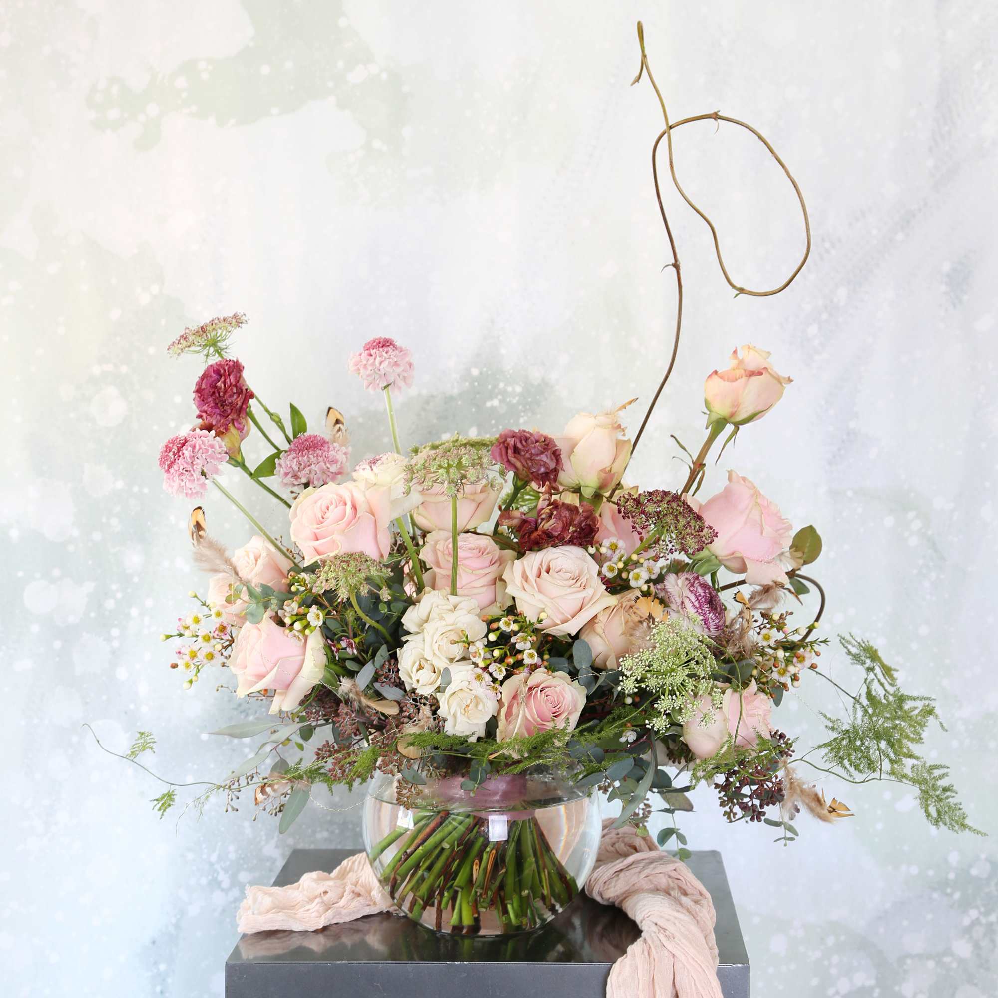 Low glass vase of blush pink and cream roses with mauve accents in an airy, asymmetrical arrangement