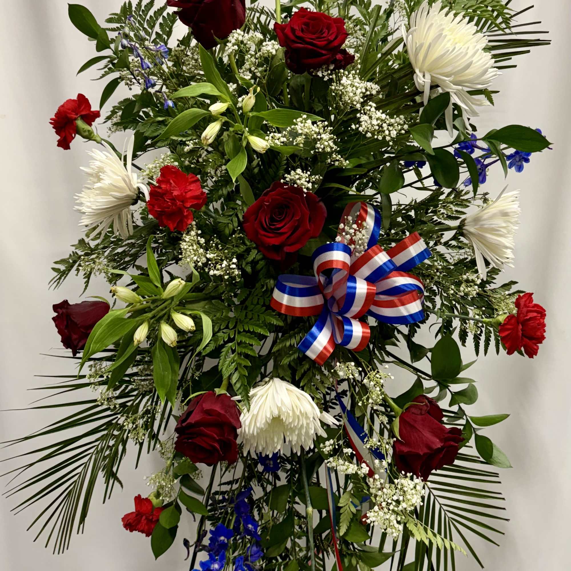 Tall floral standing spray with red roses, white mums, and blue accents on an easel.