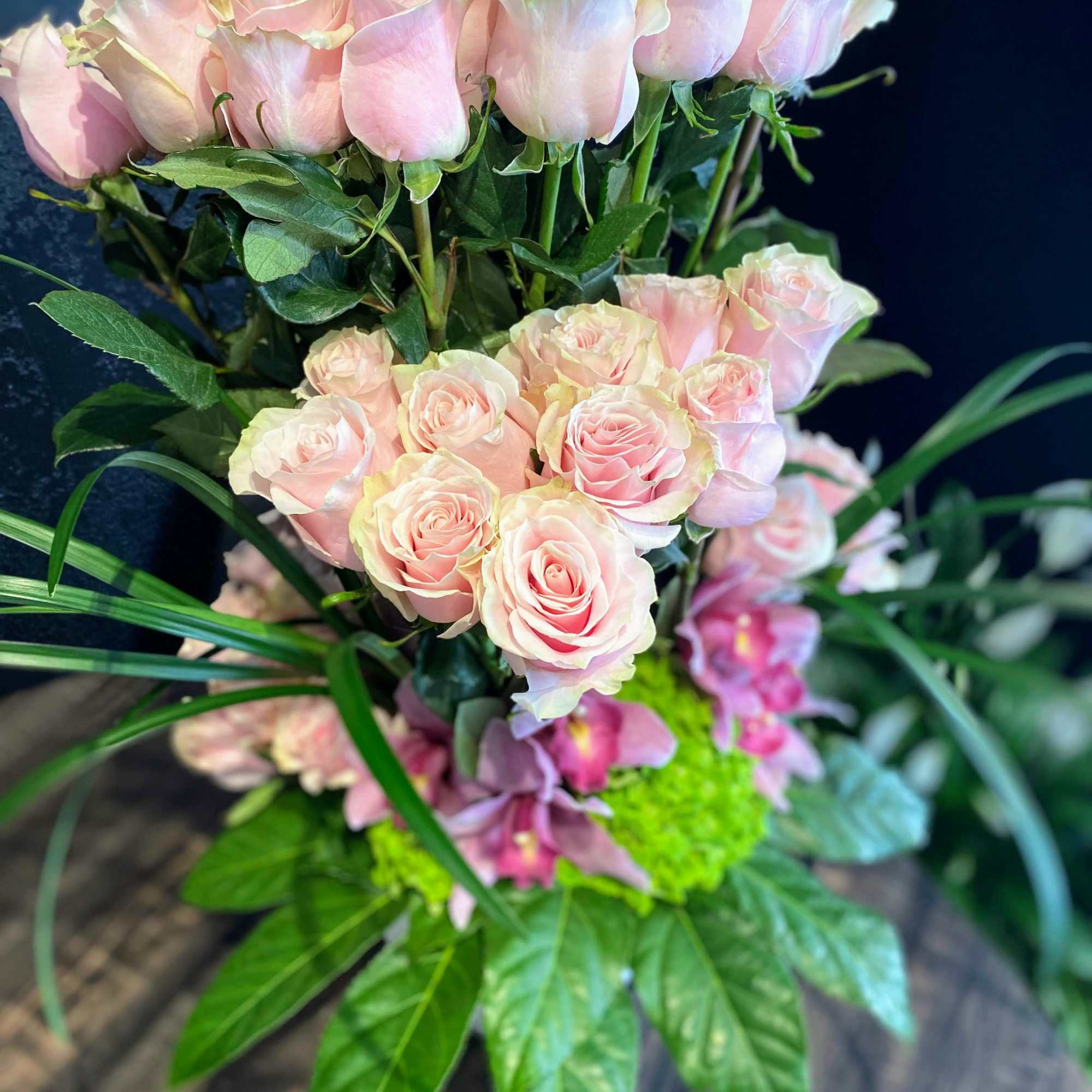 Pink roses arranged with green foliage and orchids