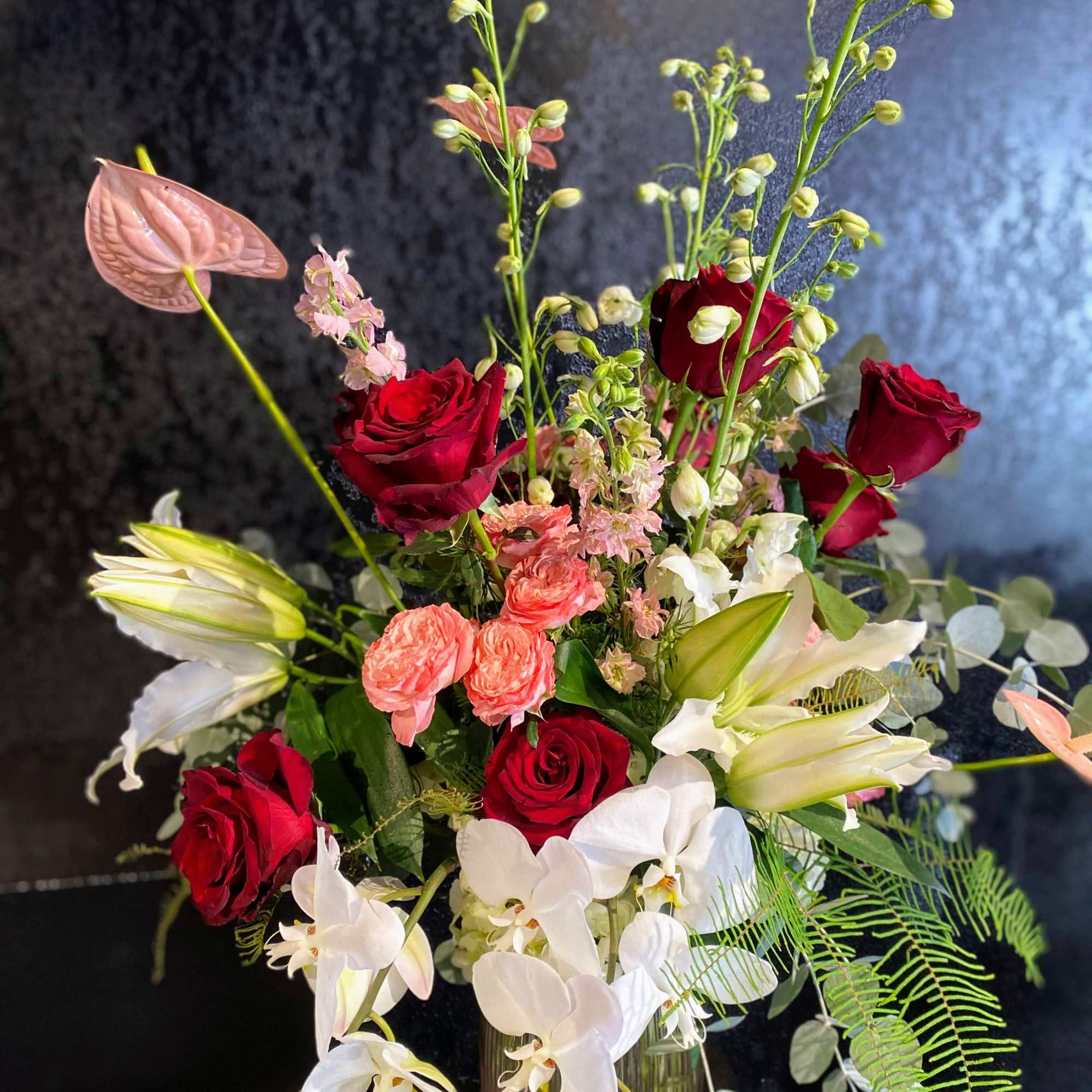 Tall bouquet of red roses, white orchids, and lilies in a vase