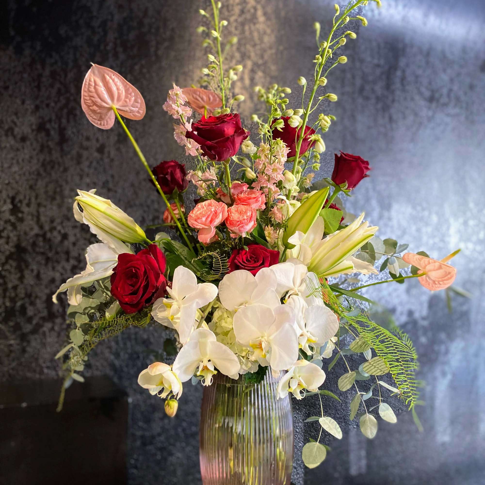 Mixed bouquet of red roses, white orchids, and lilies in a glass vase
