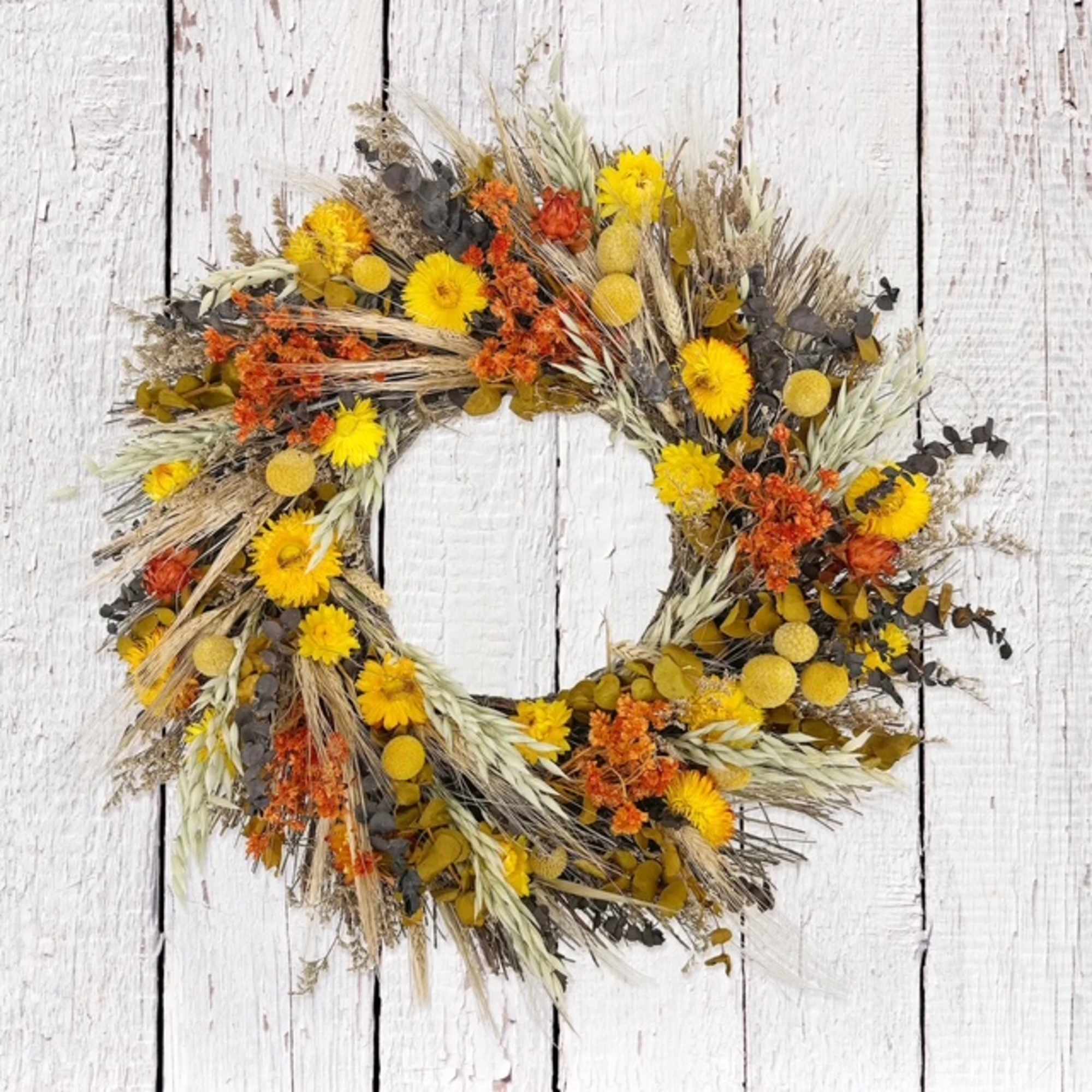 Dried floral wreath with yellow and orange blooms on a white wood background