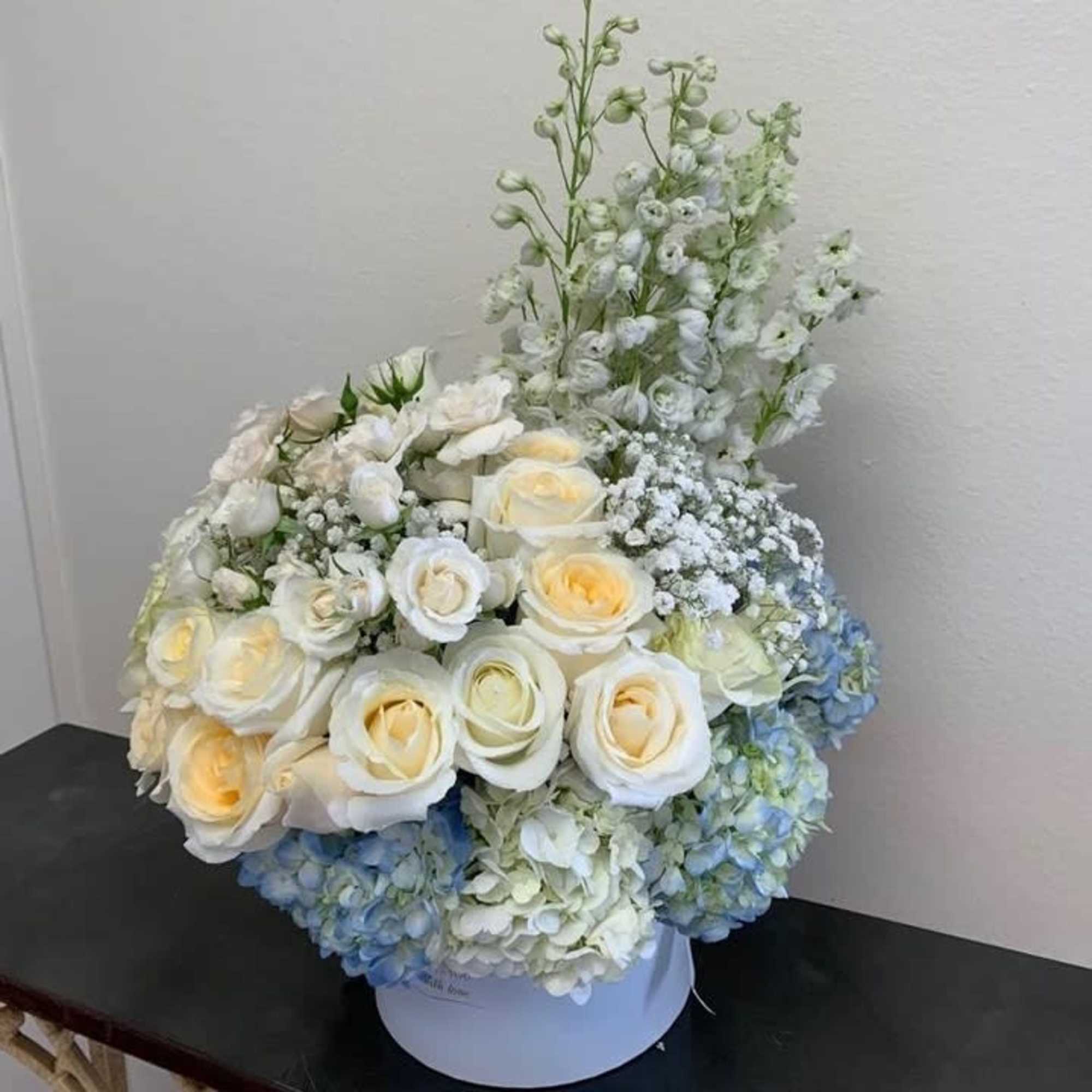 White and pale yellow roses with blue hydrangeas in a round box