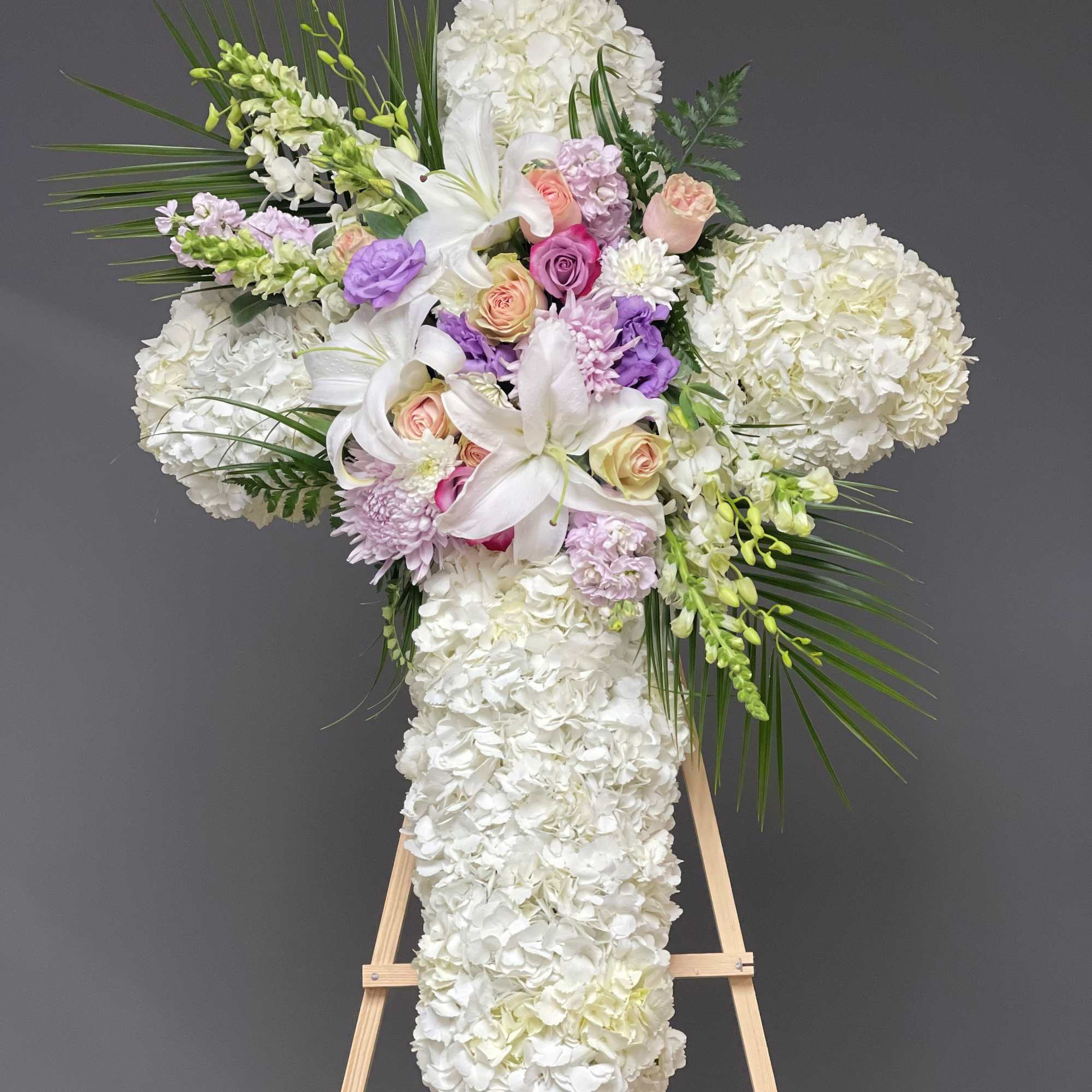 White floral cross arrangement with lilies, roses, and hydrangeas on an easel