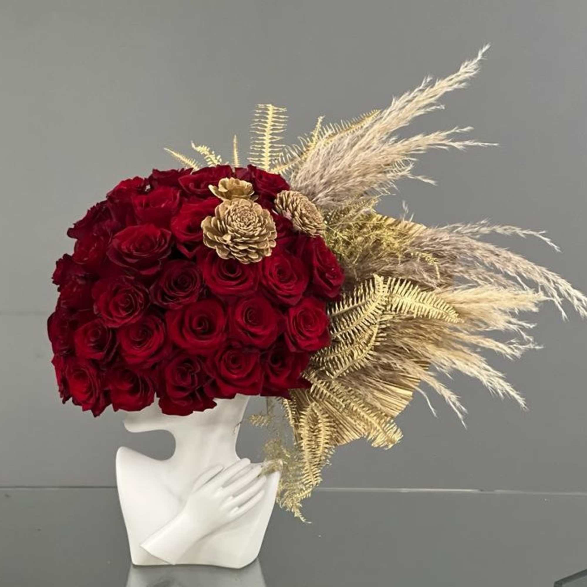 Red rose arrangement in a white sculptural vase with gold dried accents