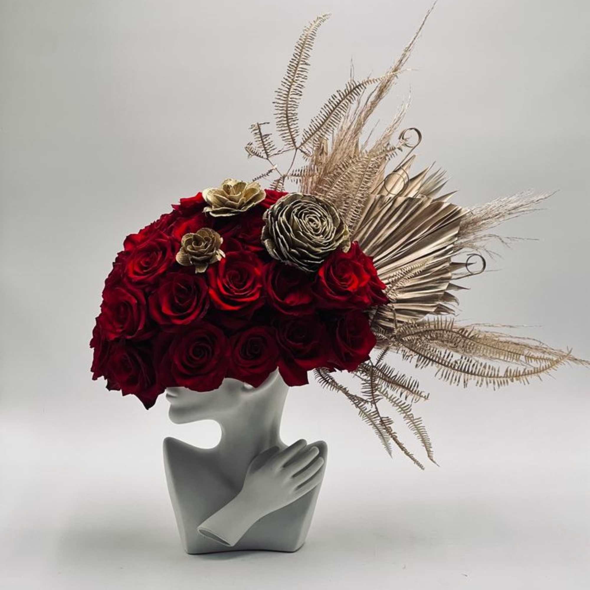 Red rose arrangement in a gray sculptural vase with gold dried accents