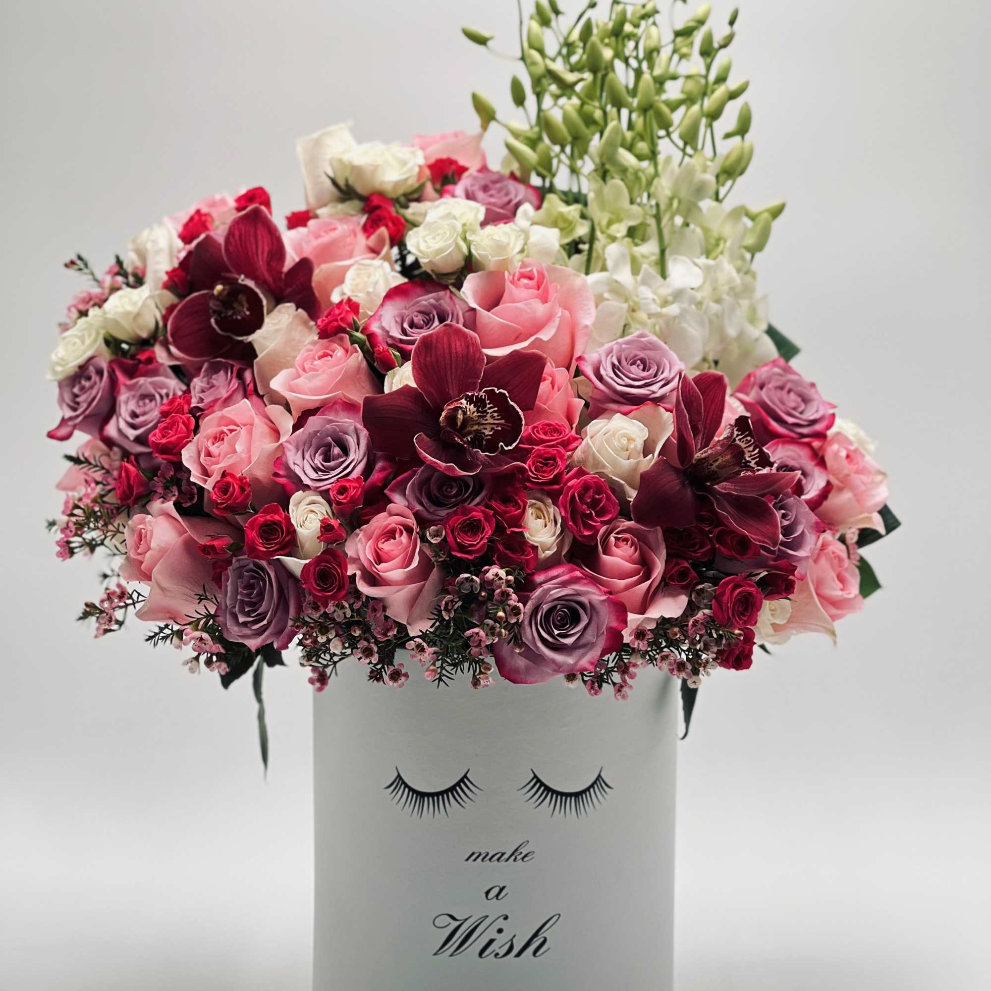 Pink, white, and burgundy flower arrangement in a white box with eyelash design