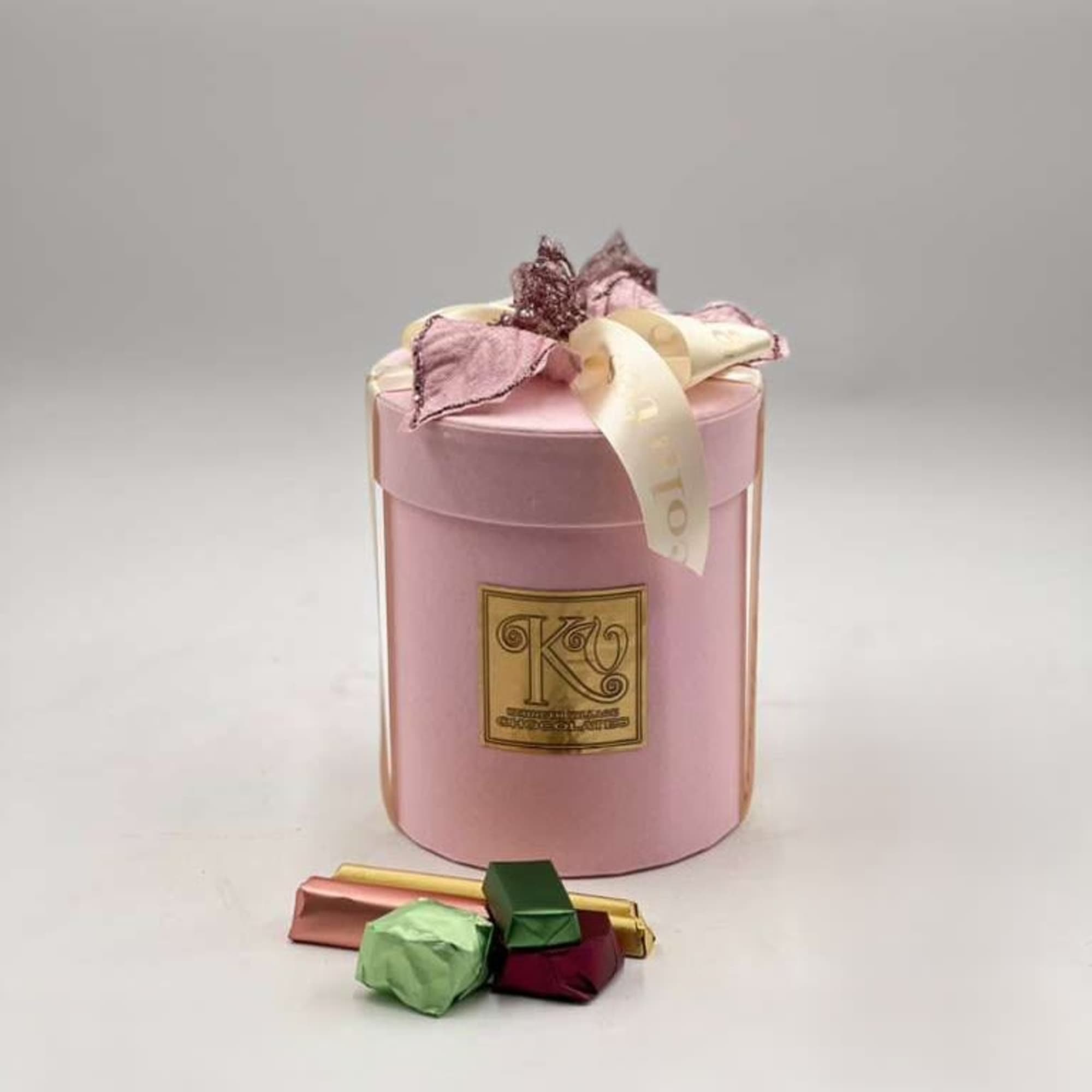 Pink gift box with ribbon and assorted chocolates in front