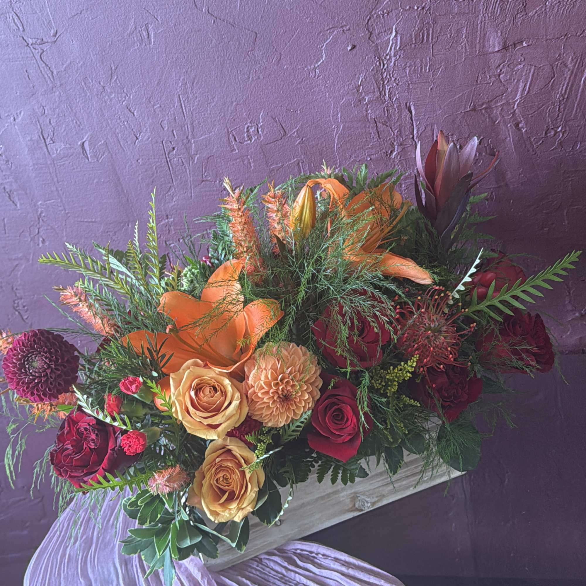 Mixed bouquet with orange and burgundy flowers in a wooden container