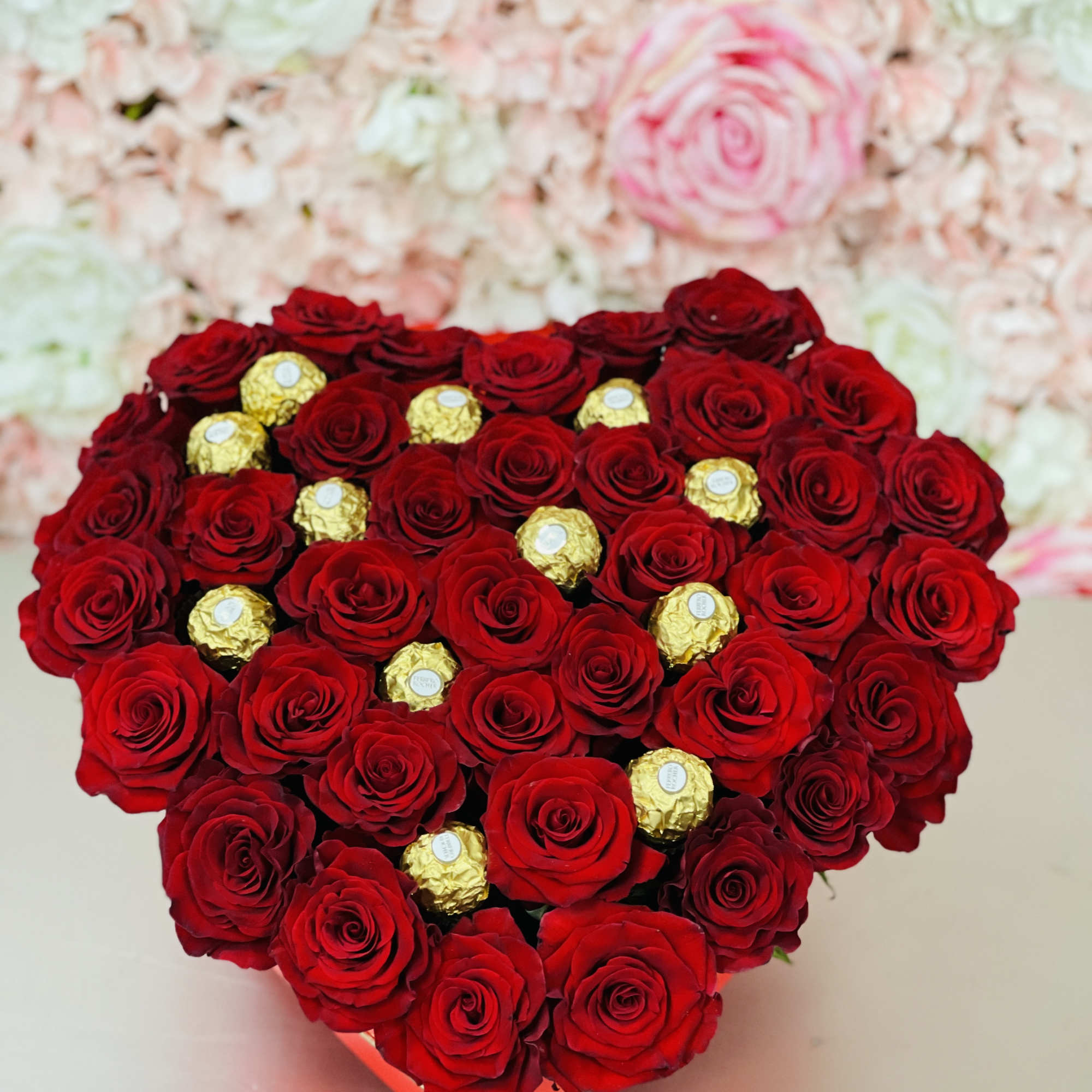 Heart-shaped arrangement of red roses with gold-wrapped chocolates in a red box