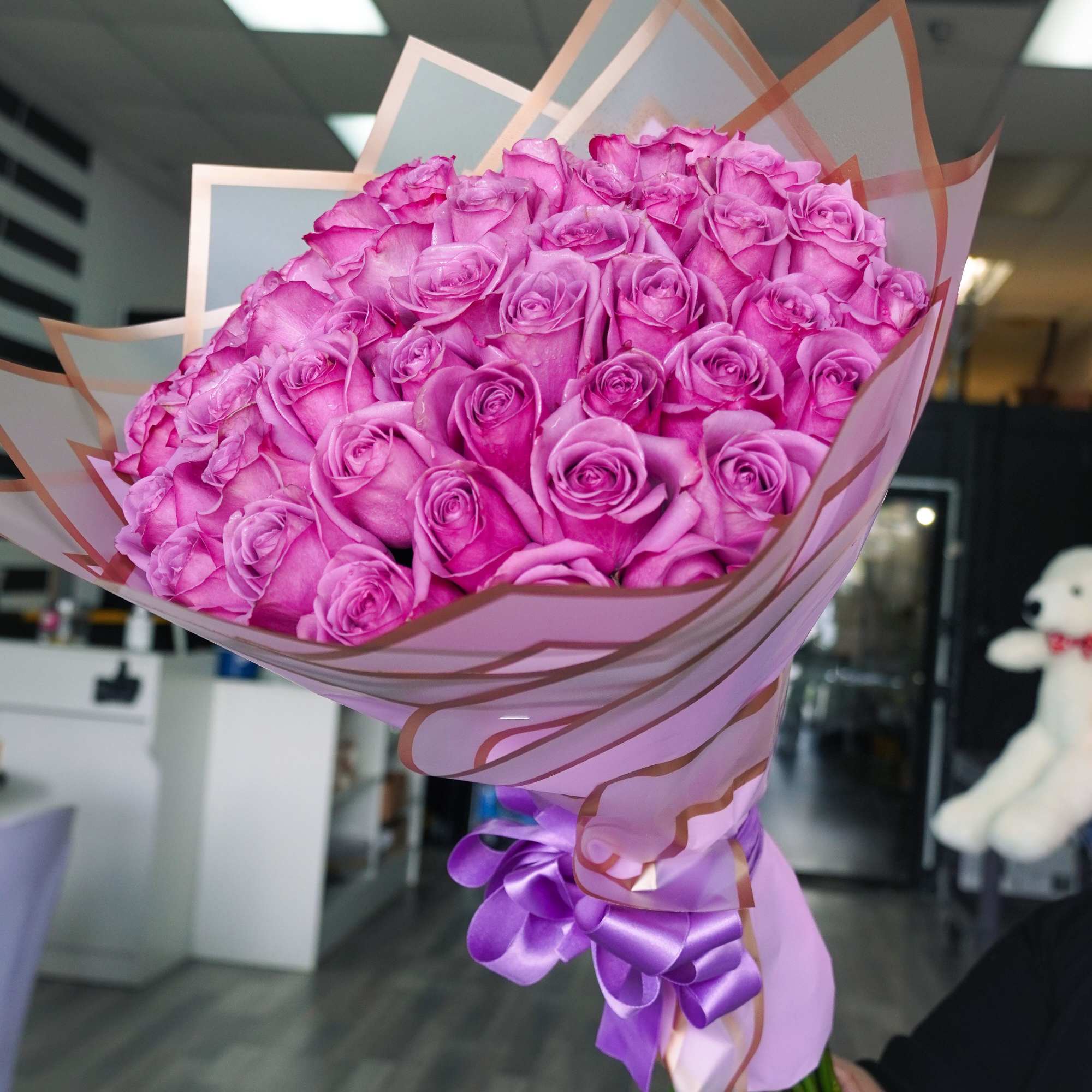 Bouquet of pink roses wrapped in pink paper with a purple ribbon