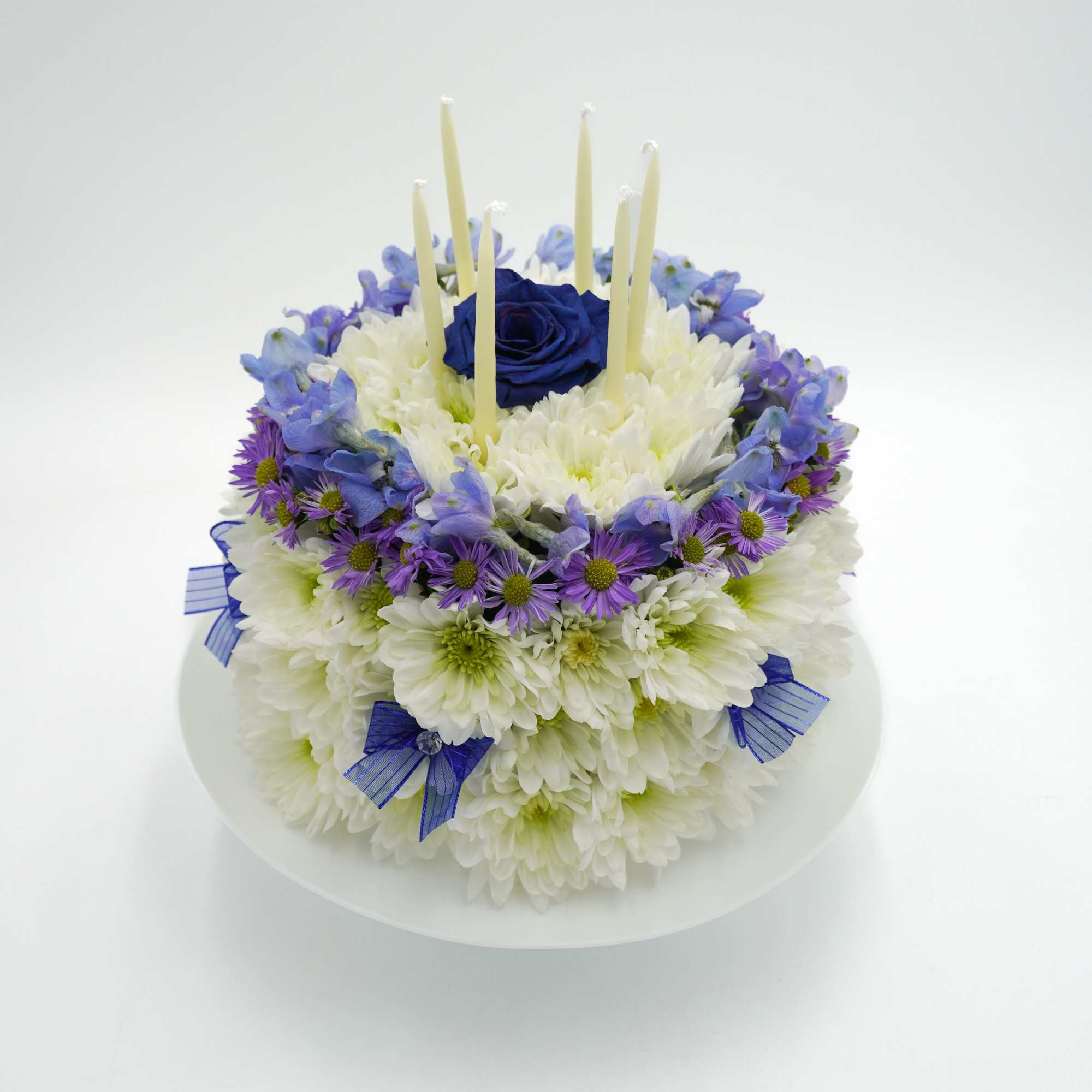 Round floral cake with white and purple flowers and tall candles
