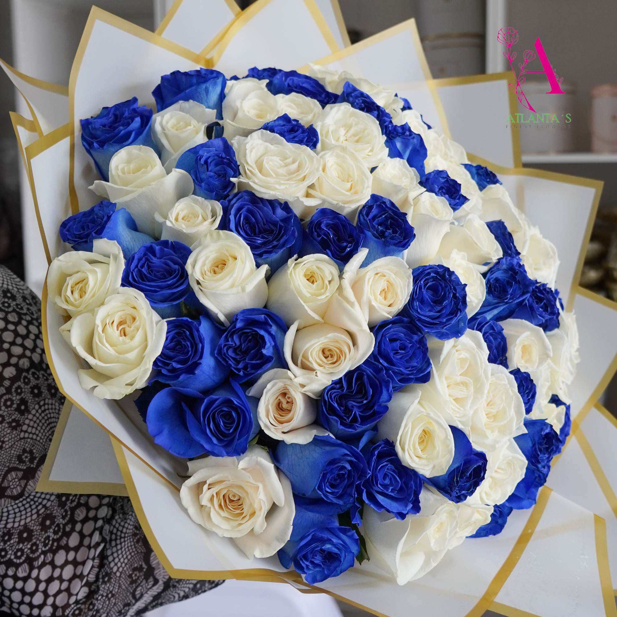 Bouquet of blue and white roses wrapped in white paper with gold trim.