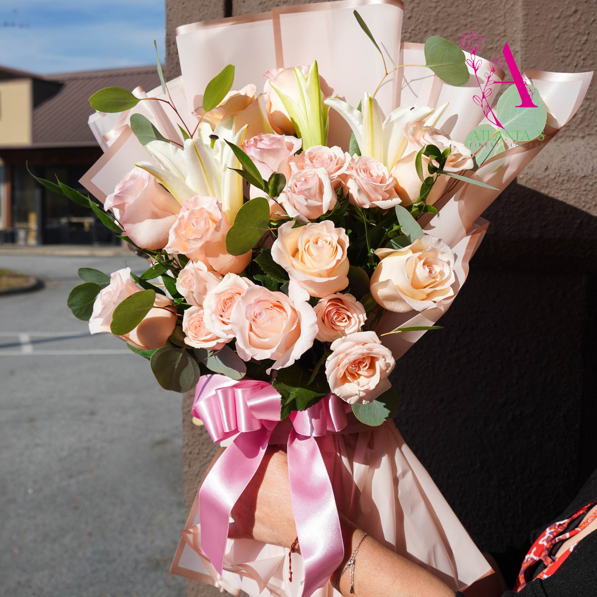 Bouquet of pale peach roses and white lilies wrapped in pink paper
