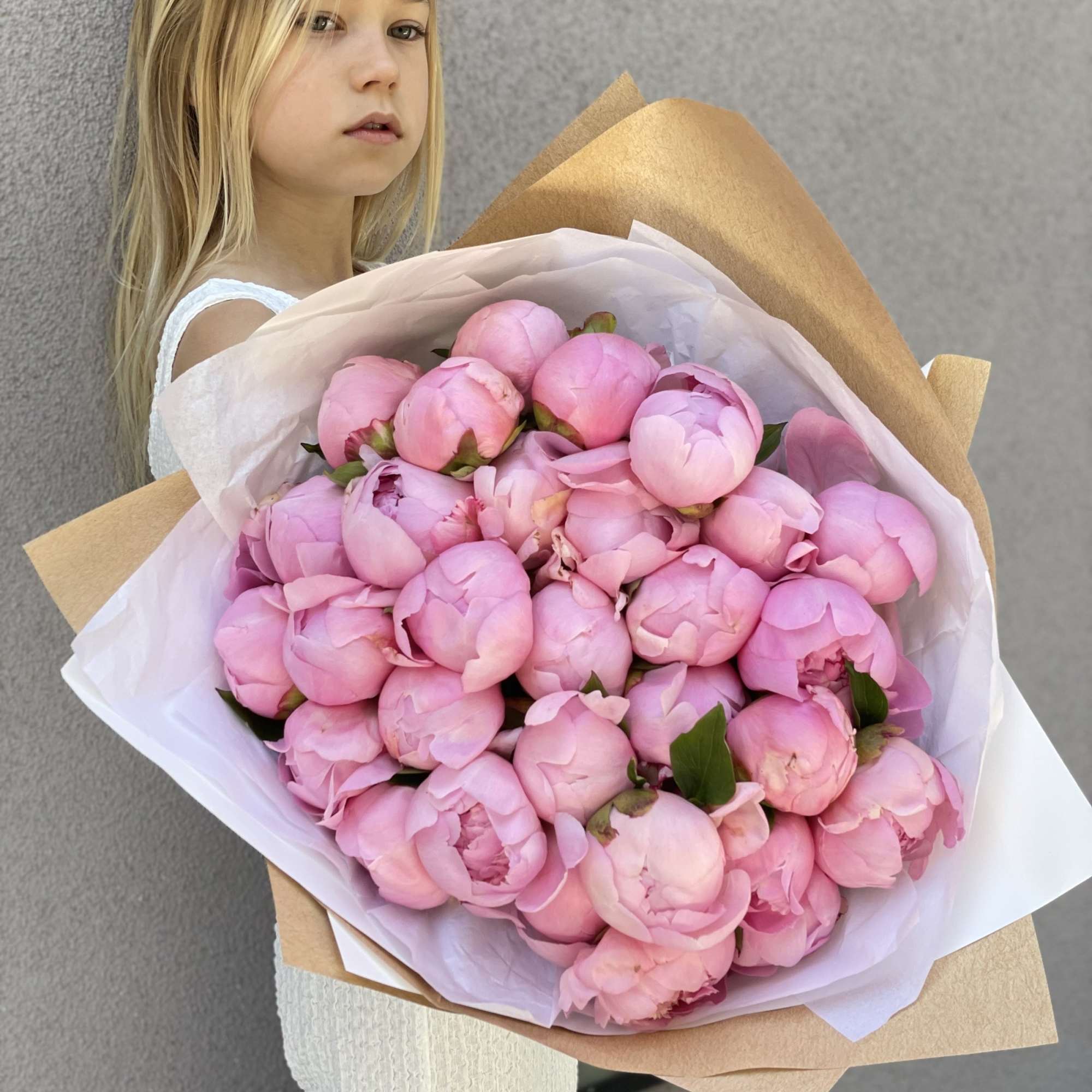 Girl holding a large bouquet of pink peonies wrapped in paper