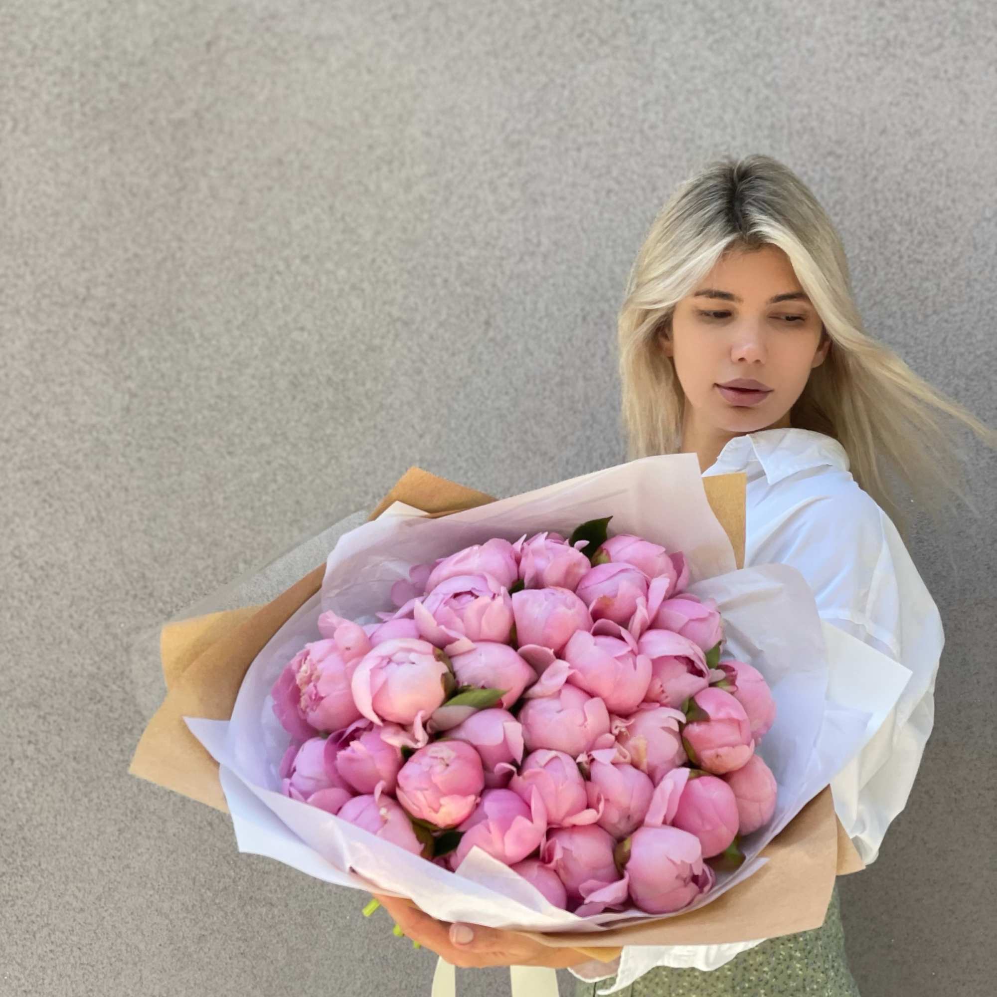 Woman holding a large bouquet of pink peonies wrapped in white and kraft paper
