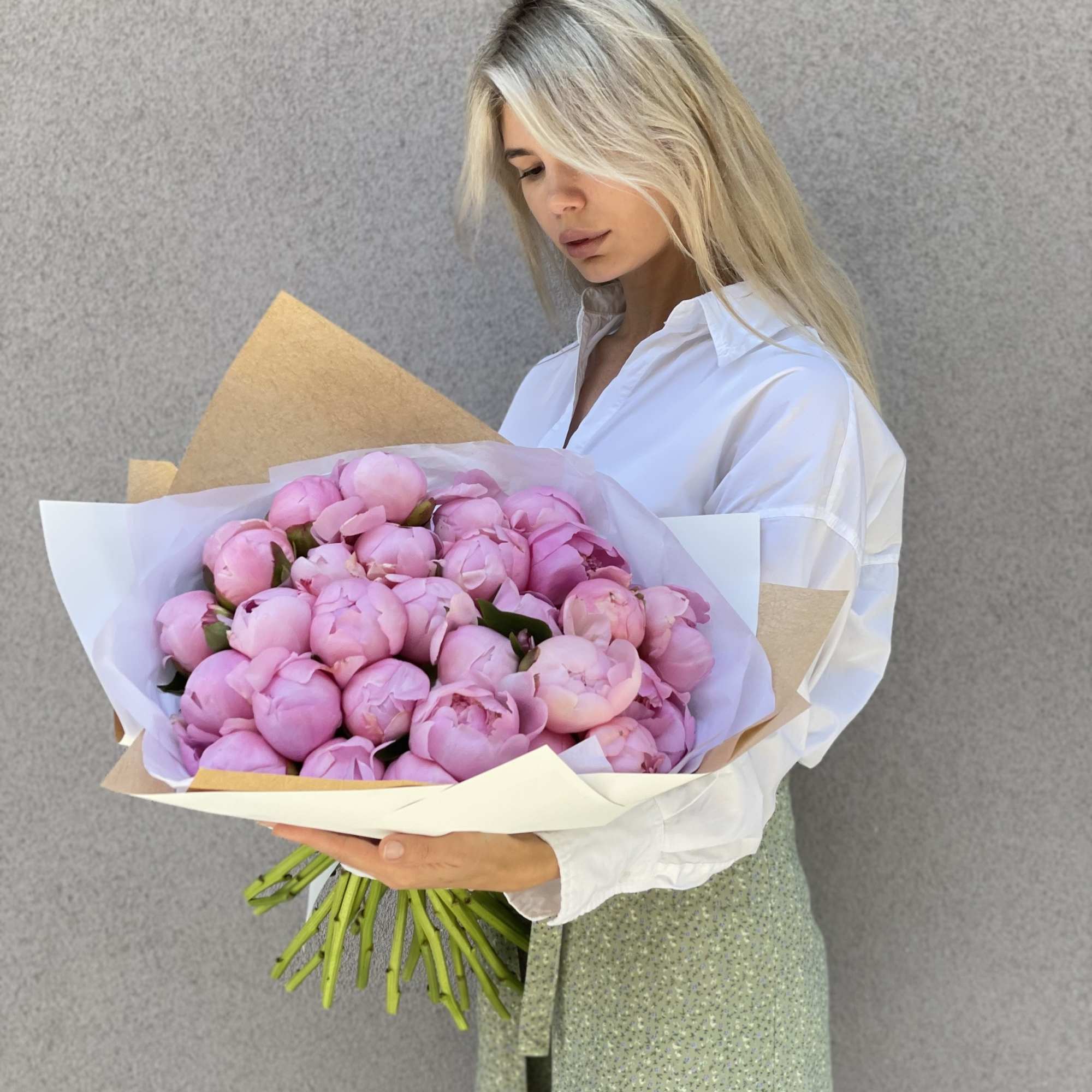 Woman holding a large bouquet of pink peonies wrapped in white and tan paper