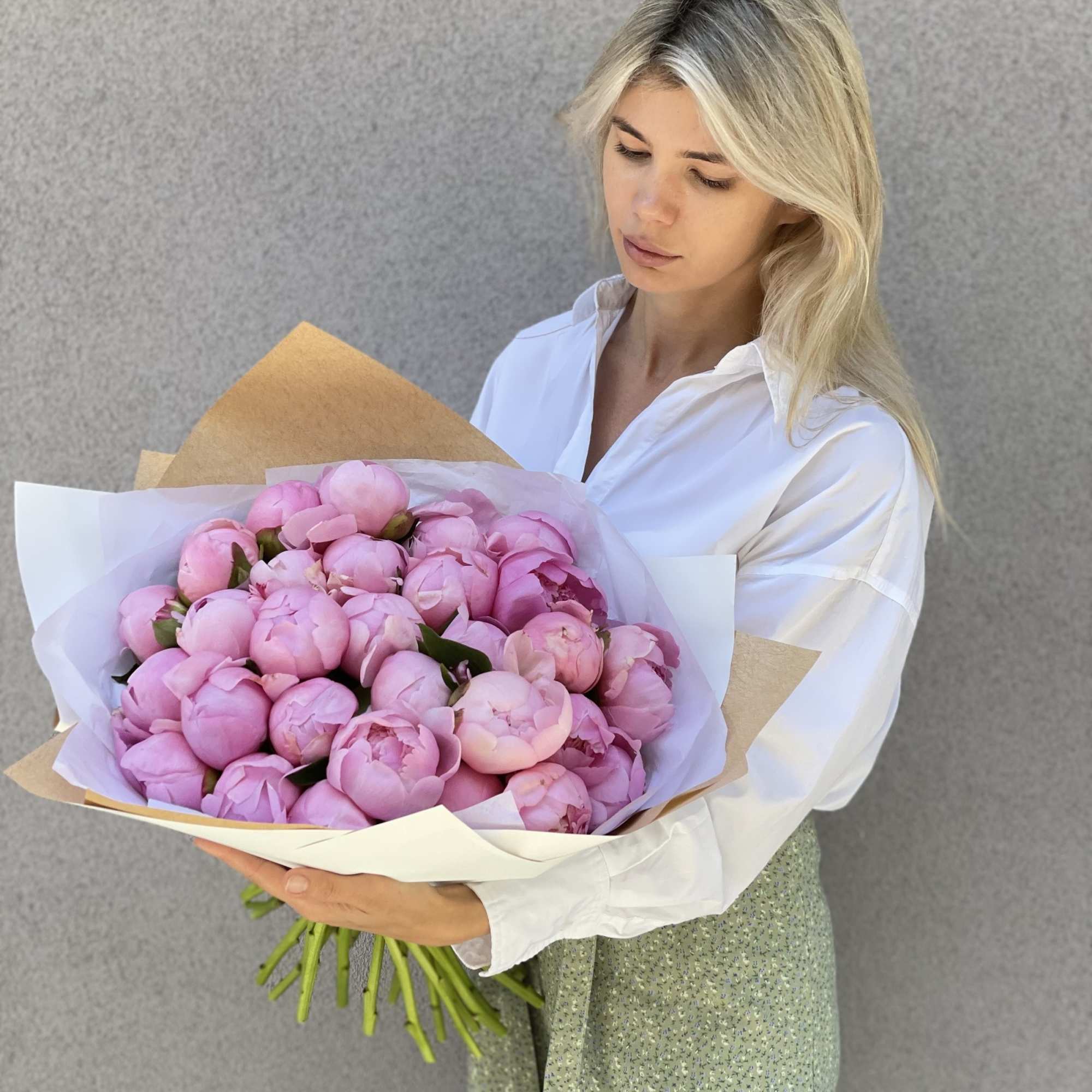 Woman holding a bouquet of pink peonies wrapped in white paper