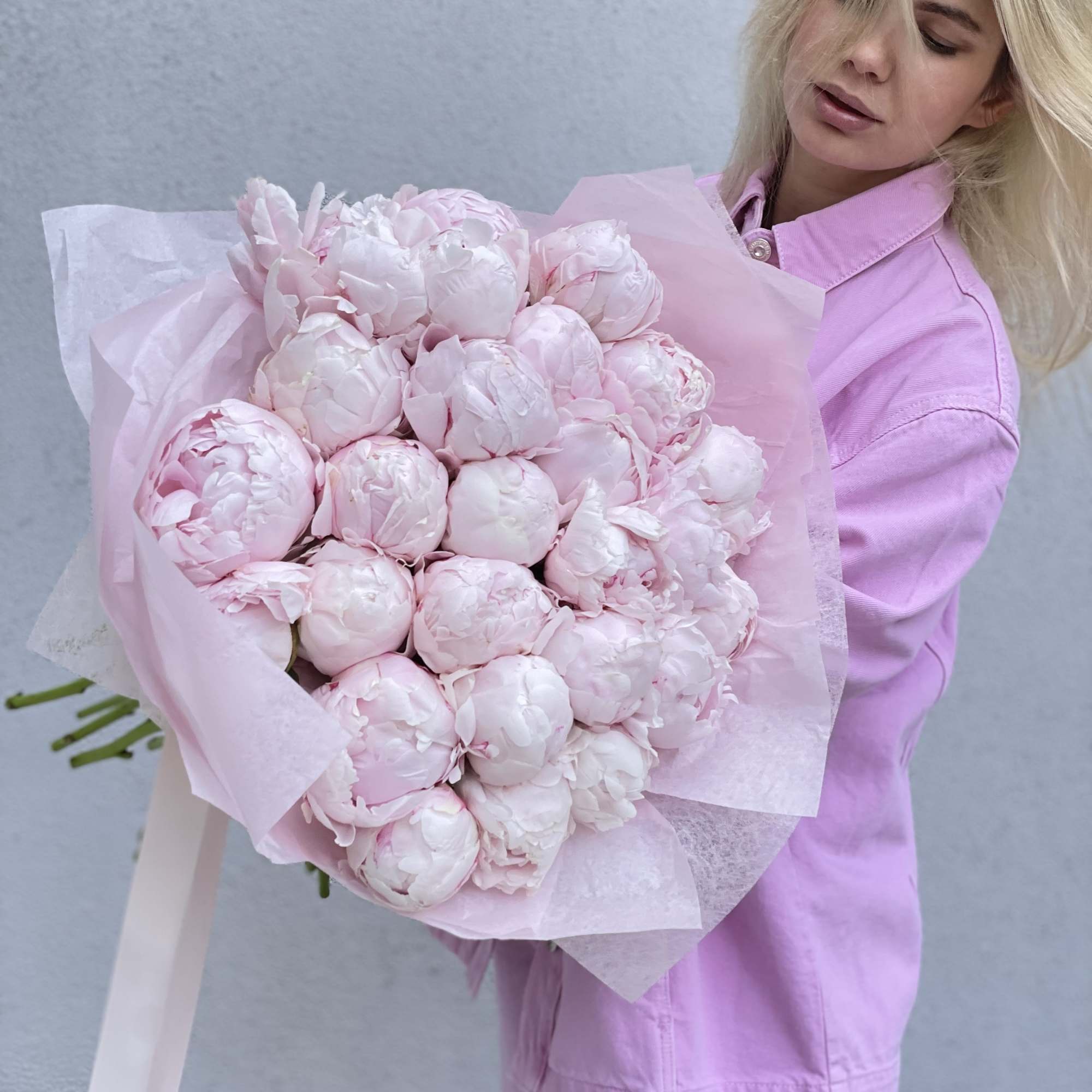 Woman holding a large bouquet of pale pink peonies wrapped in pink paper