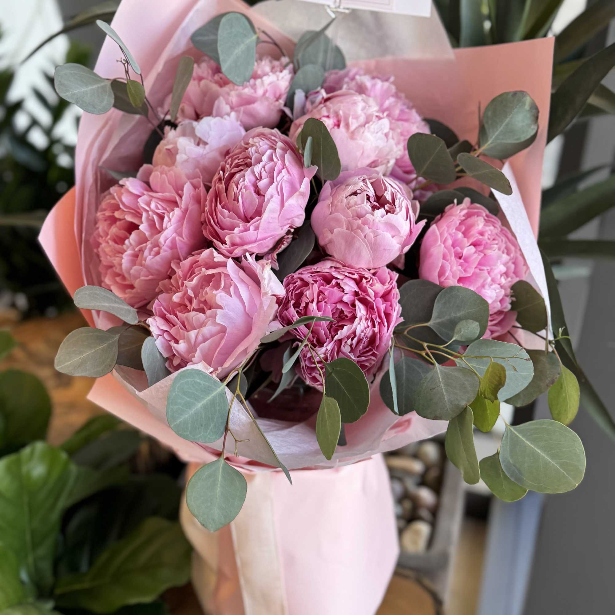 Pink peony bouquet wrapped in pastel paper with eucalyptus