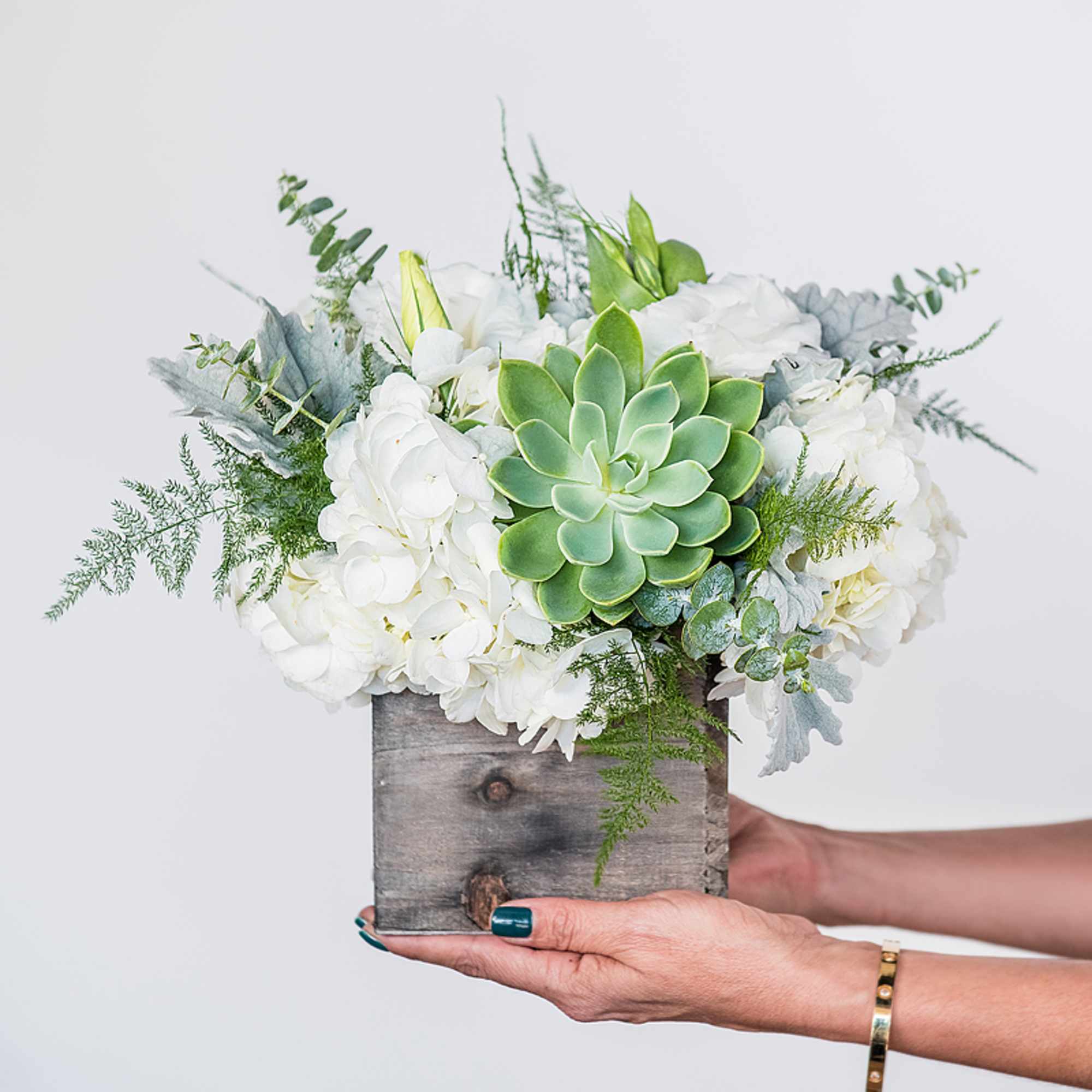 White floral arrangement with a green succulent in a rustic wooden box