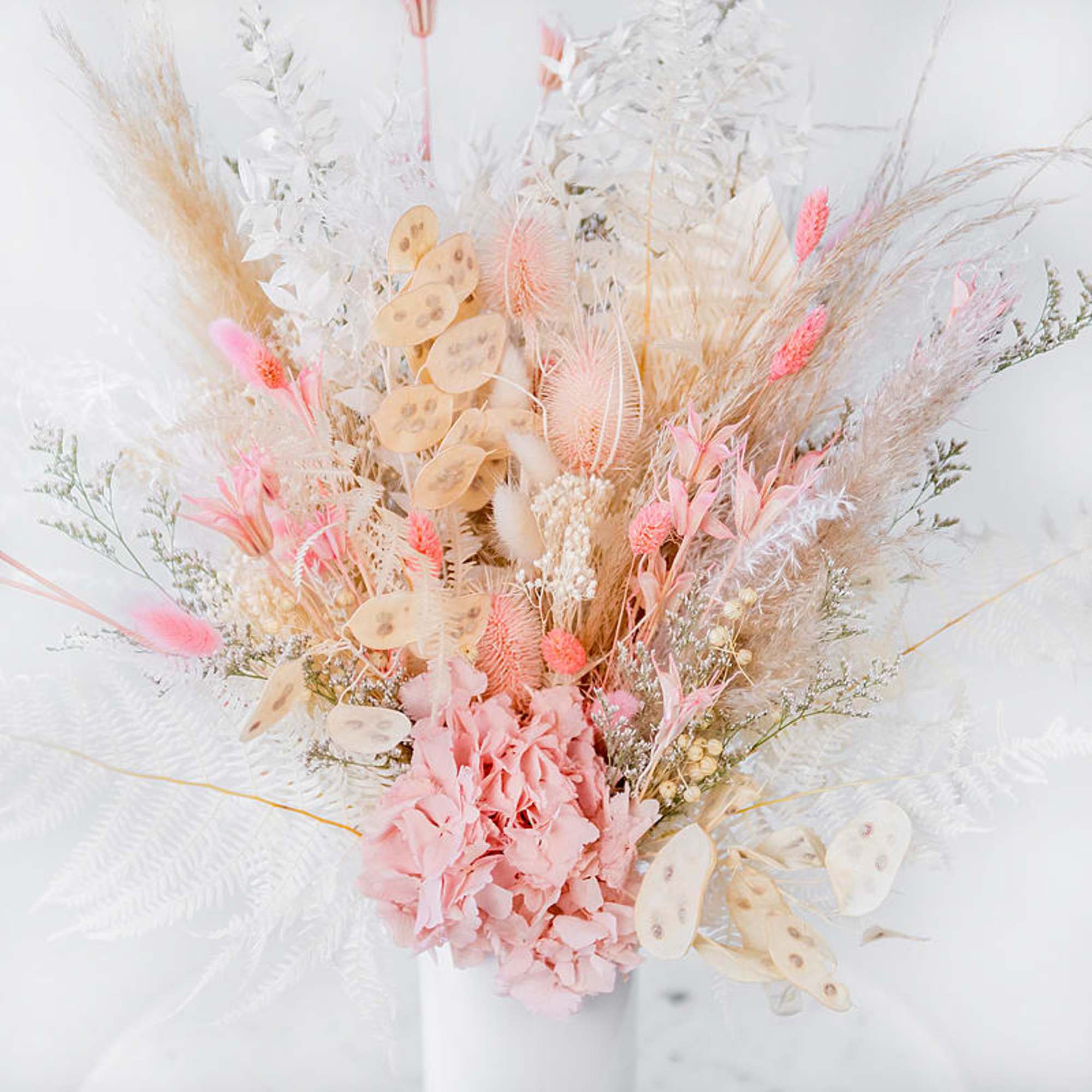 Dried bouquet with pink flowers and white pampas grass in a white vase