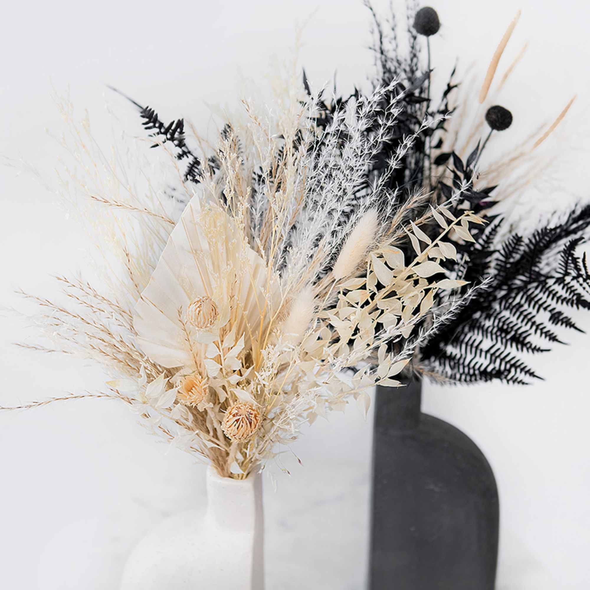 Dried floral arrangement in a white vase with cream and black accents