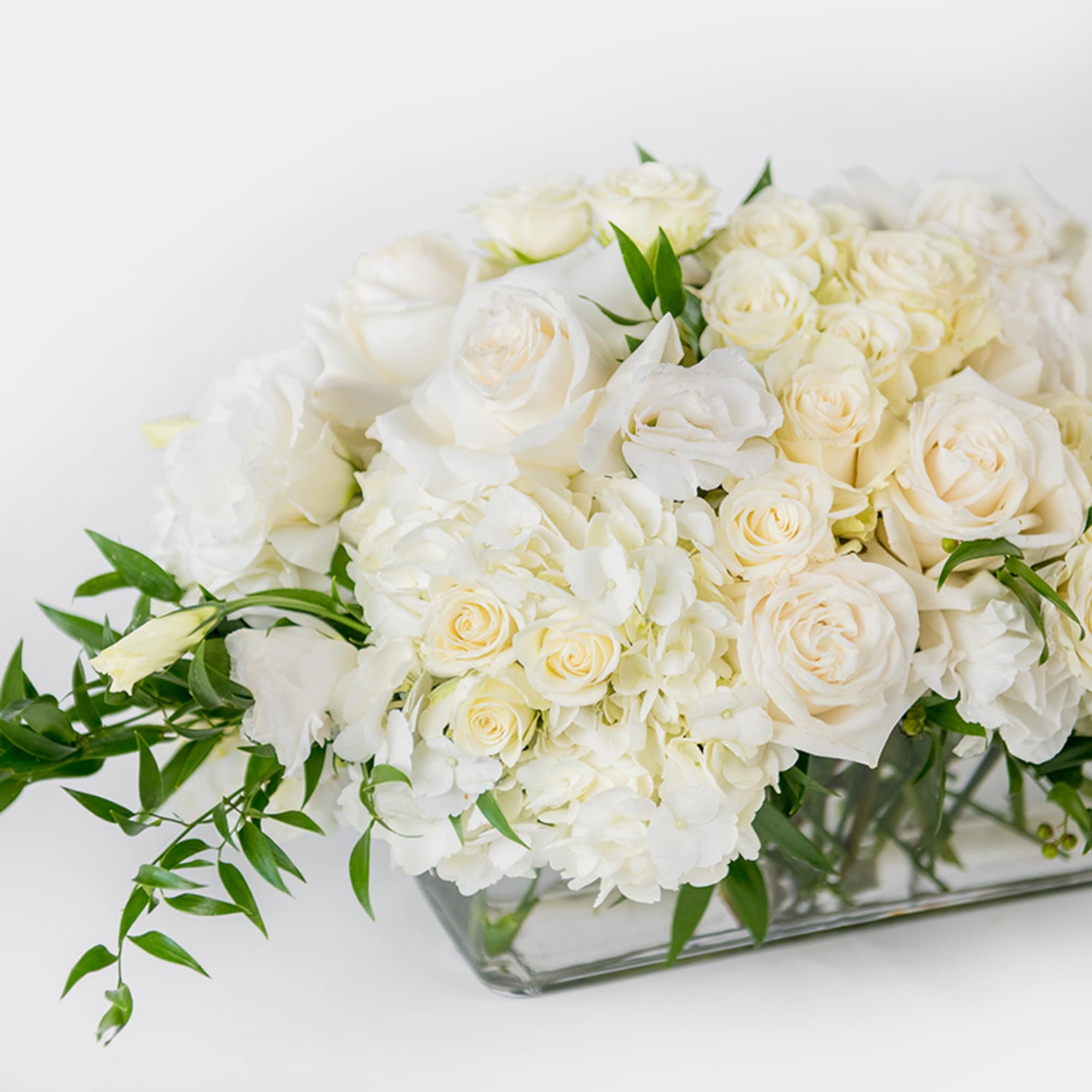 Low white and cream rose and hydrangea arrangement in a rectangular clear glass vase