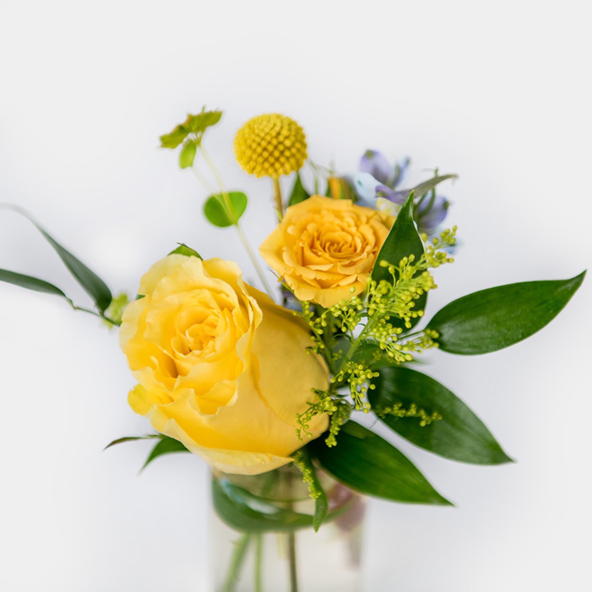 Small arrangement of yellow roses with a round yellow accent flower in a clear glass vase